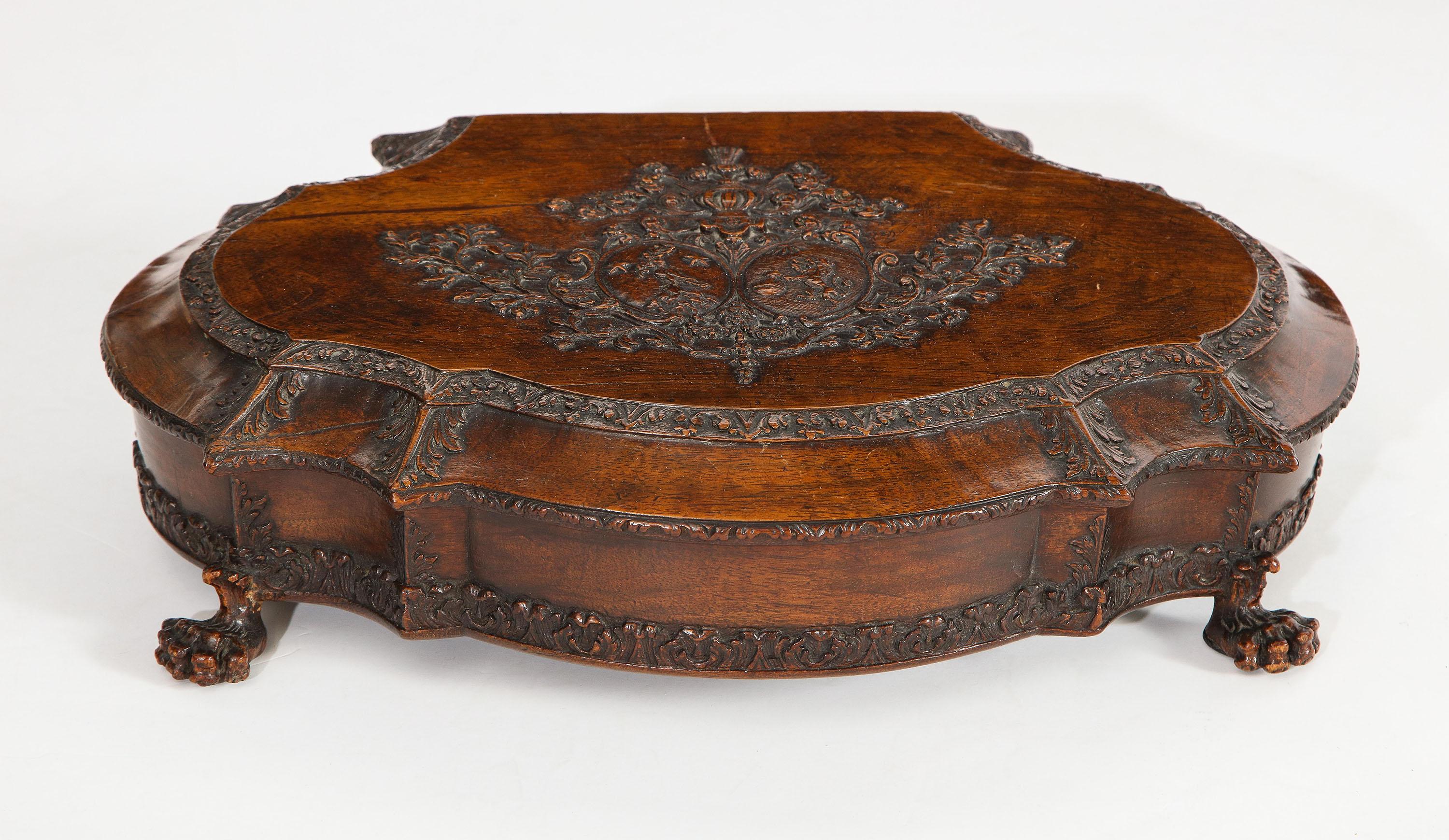 The elaborate ovoid form walnut box with lid showing royal coat of arms carved in relief, acanthus leaves at stylized points and opens to reveal an incised design on cover, all on paw feet