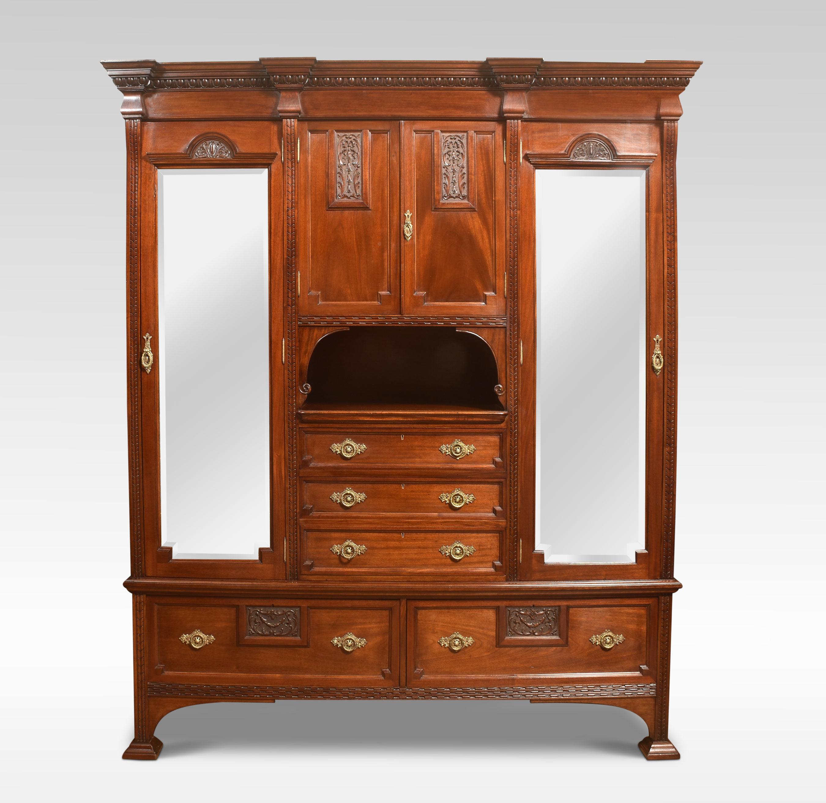 Carved mahogany compactum wardrobe having carved removable finials, above two long mirror doors flanking the centre fitted with a pair of carved panelled doors and three drawers below. To the base section fitted with two large drawers having brass