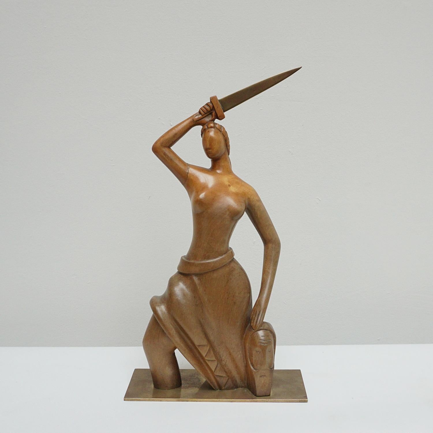 Eine Art-Déco-Skulptur des ungarischen Designers Laszlo Hoenig (1905-1971). Eine geschnitzte Holzstudie einer stilisierten halbnackten Figur, die ein Bronzeschwert und eine Stammesmaske hält. Hochglanzpolierter Nussbaum auf einem Bronzesockel. Auf