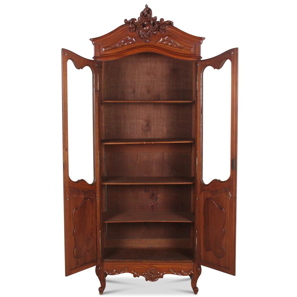 An unusually narrow two-door Louis XV style bookcase with an elaborately-carved crown and carved walnut panels to the lower doors.