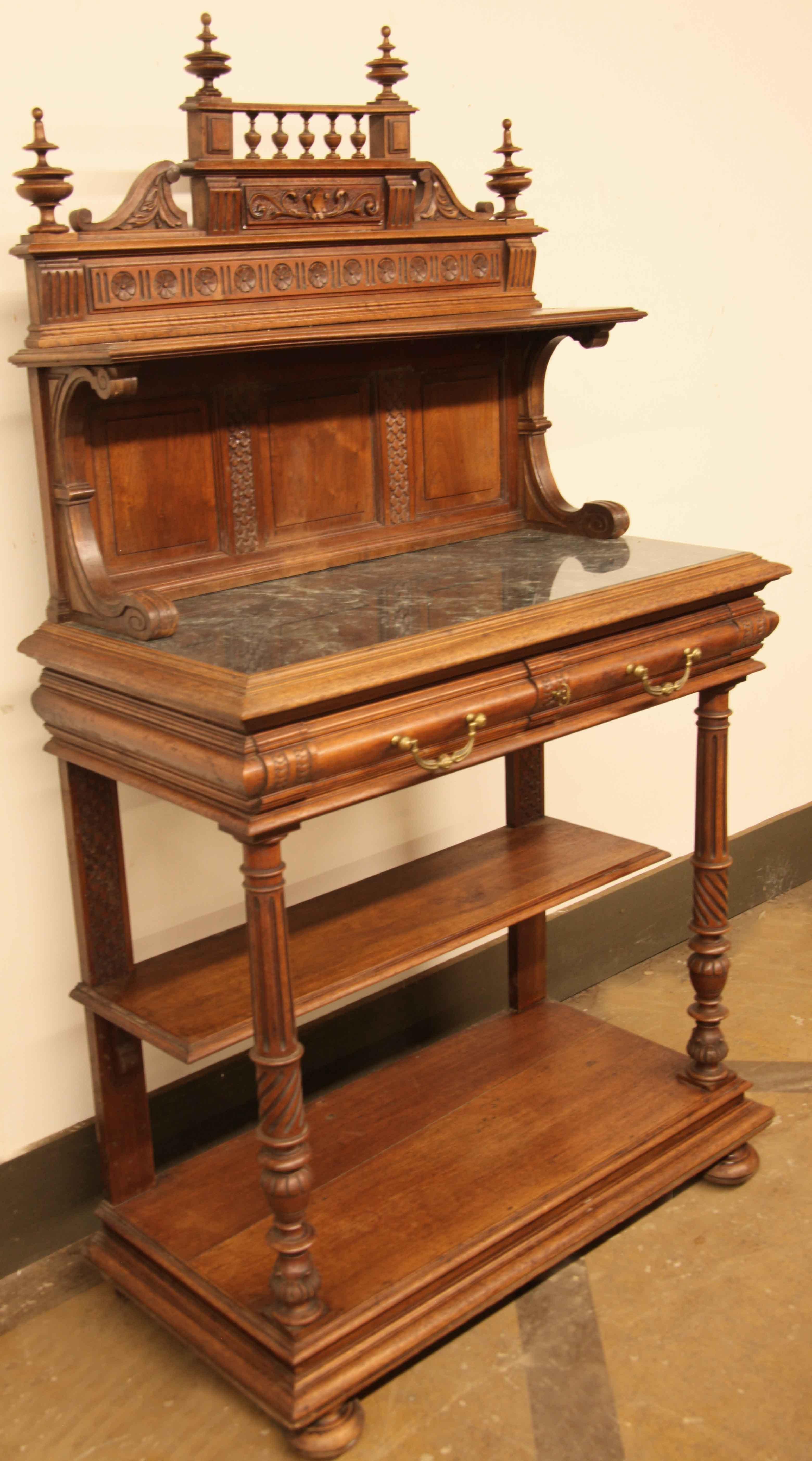 Carved walnut marble top sideboard, the back gallery features pediment with four turned finials and spindles above cartouche with shield, arabesques and stippling, followed by a horizontal row of carved rosettes and 9'' deep shelf.  Below this are