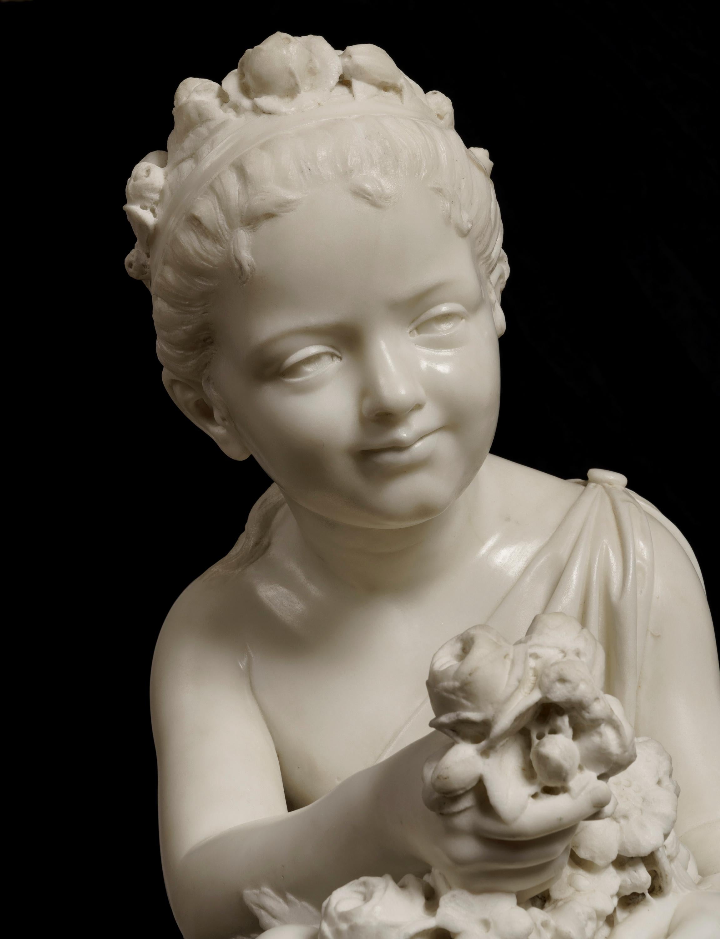 A carved white marble figure of a flower girl
Signed to base 'Monti'

Modelled as a young girl, dressed in a classical toga with generous billowing folds, sat on a rocky outcrop holding a basket of flowers, with one hand outstretched offering a