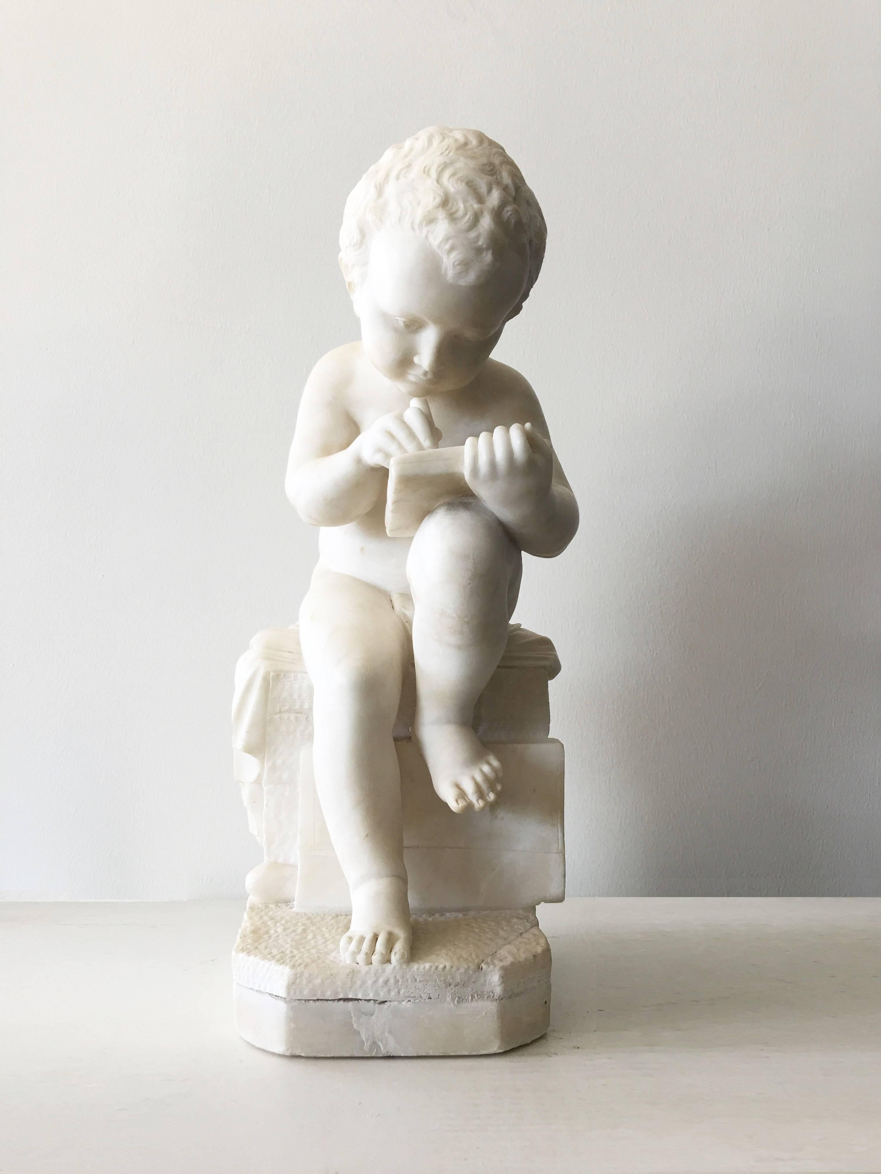 A finely carved marble sculpture. Featuring a figural sculpture featuring a young boy seating on a brick wall, a foot on a book. He is leaned over his drawing tablet. The precision of its details, especially of the hair, lend to its distinctive