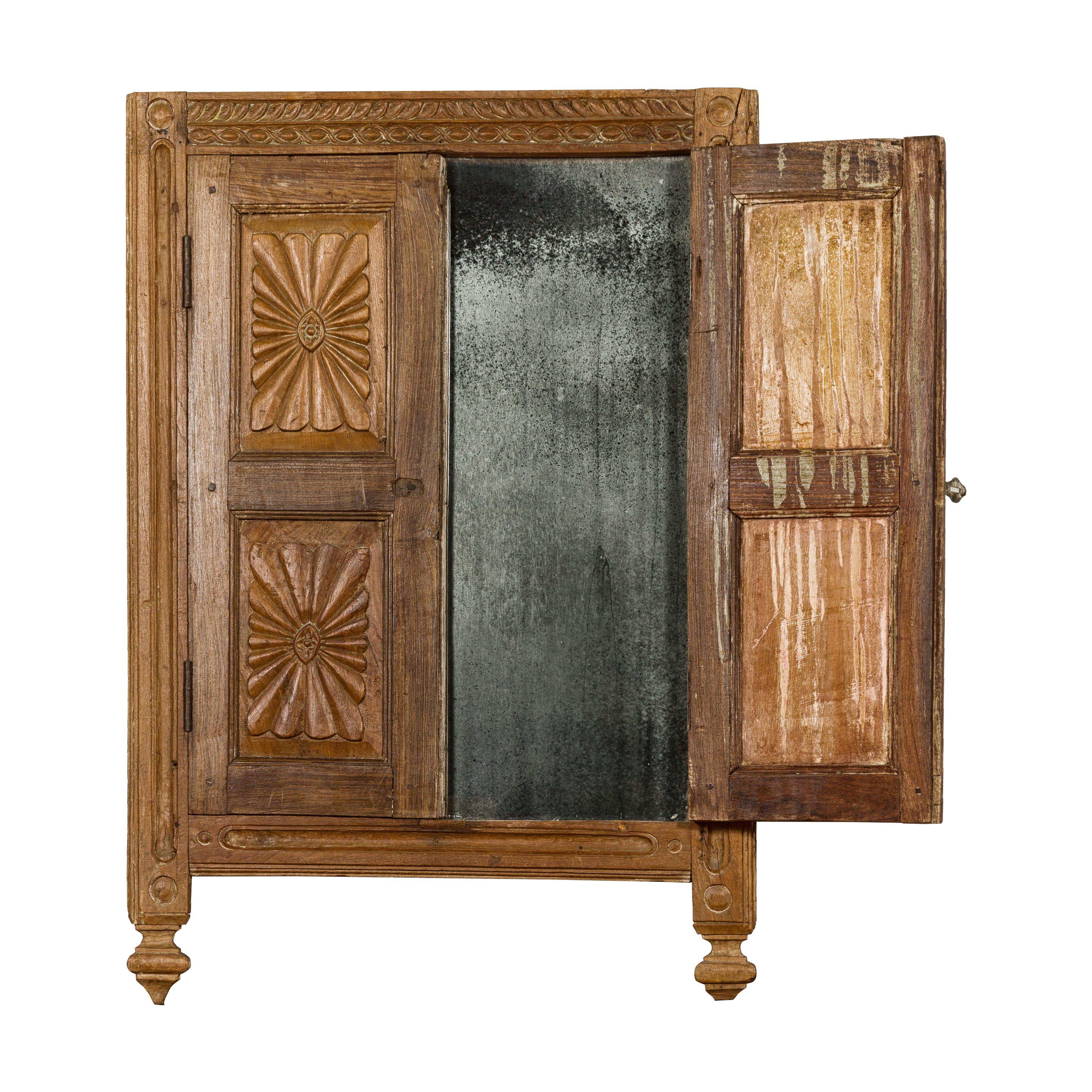 An antique Indian carved wooden window retrofitted with a smoky heavily antiqued mirror. This antique Indian carved wooden window, thoughtfully retrofitted with a smoky, heavily antiqued mirror, is a captivating piece that merges history with