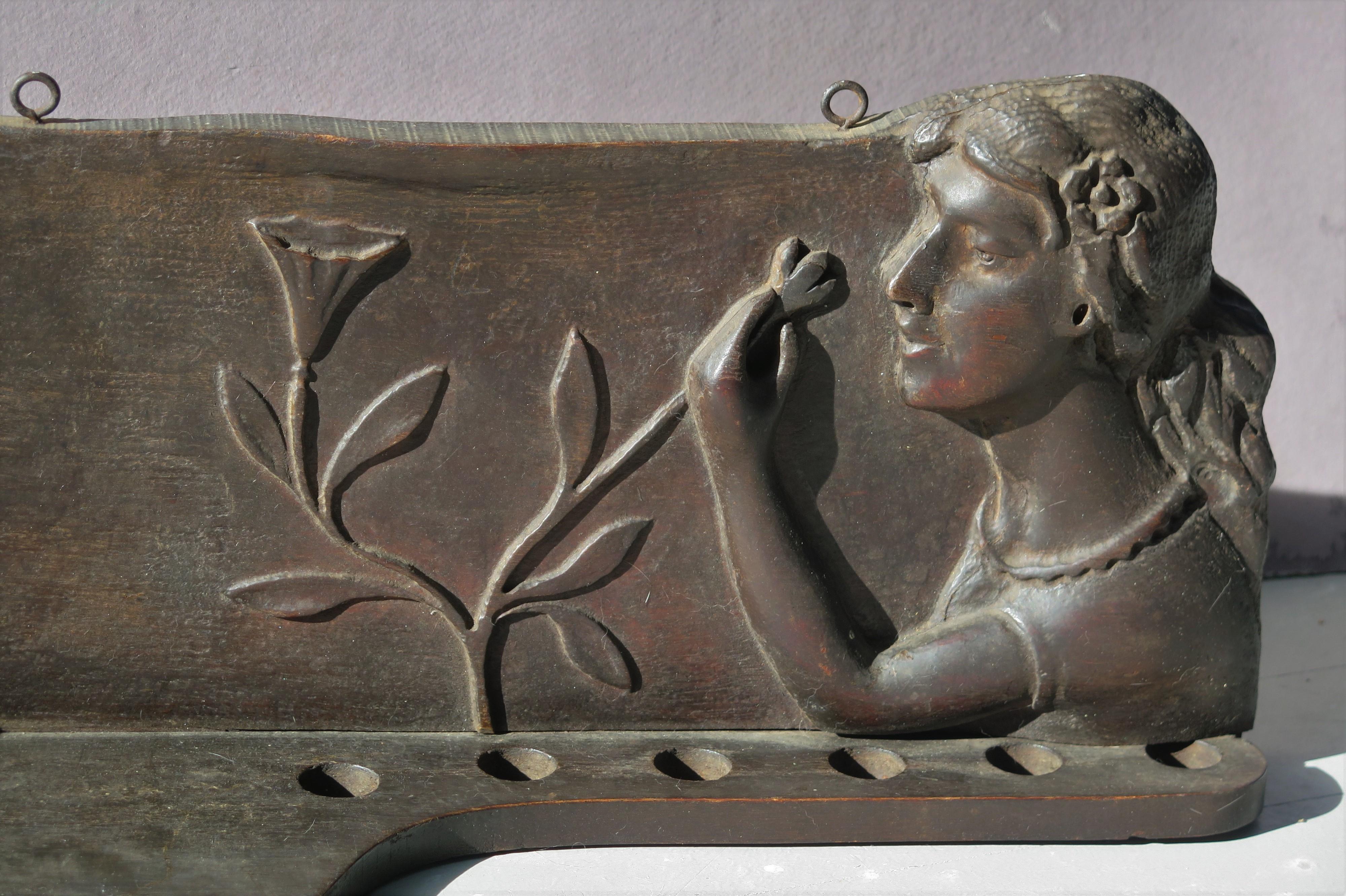 Carved and stained wood pipe shelf with a woman in relief reaching over to look at and smell the flowers. The wall piece has room for small things like keys as well as having 5 holes made for pipes but useful for other things. There is a small