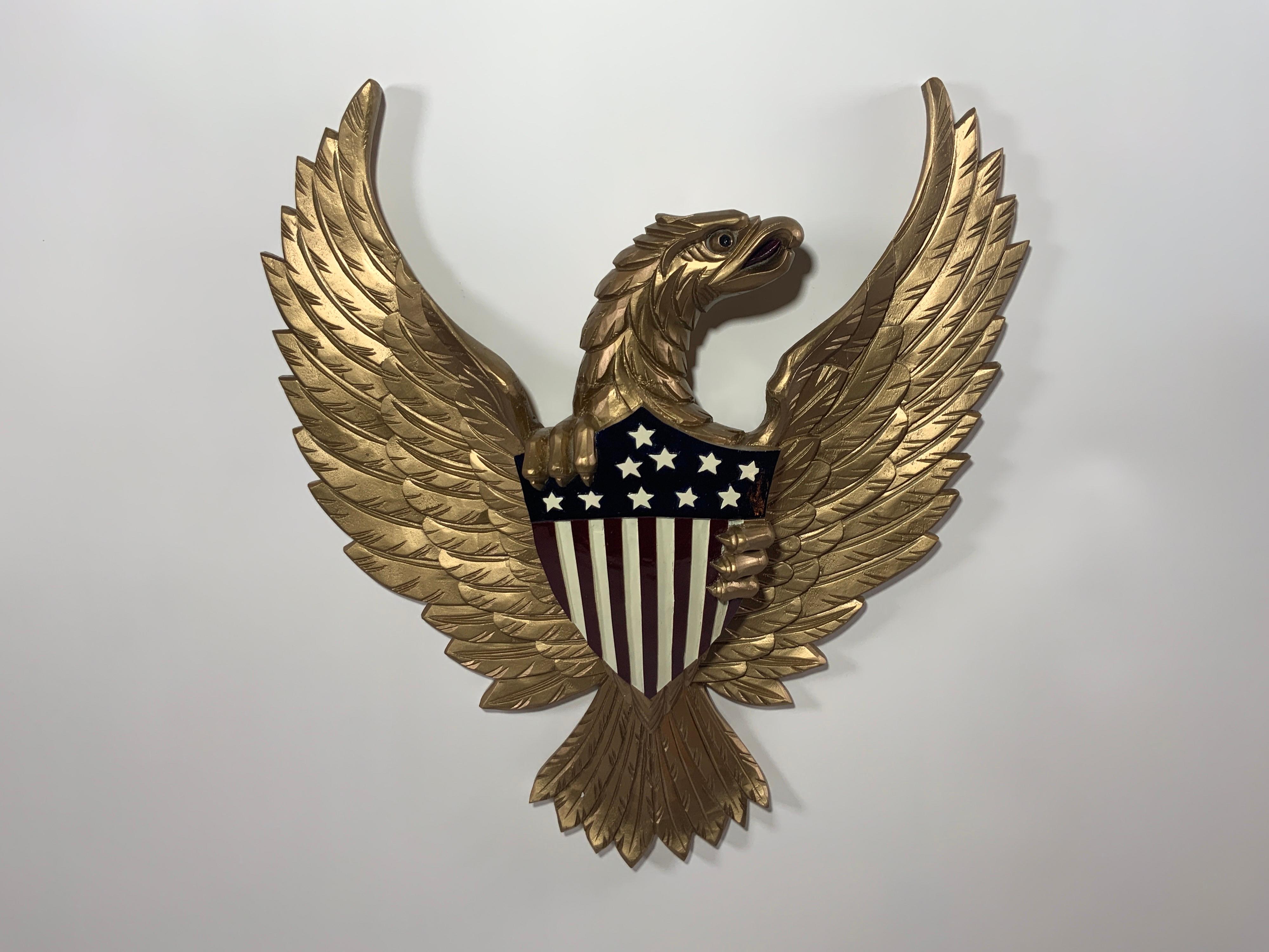 Carved wooden eagle painted with an old gold finish. Eagle is very detailed and clutching the Great Seal in the likeness of the US Coat of Arms. Rear hanging wire.

Overall dimensions: 21