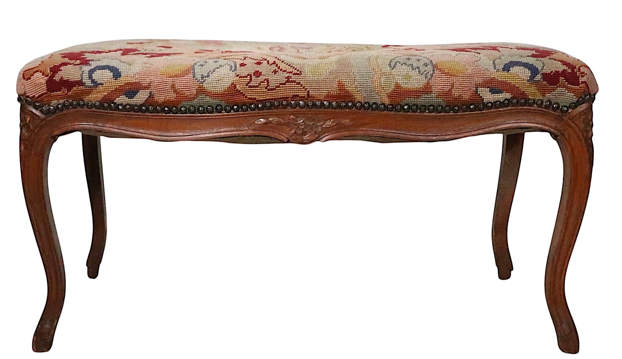 Louis XV style carved wood bench with decorative needlepoint upholstered tapestry seat and nailhead trim. The frame features elegant cabriole  legs, with carved flowers and foliate trim. This example is in good, original, ready to use condition,