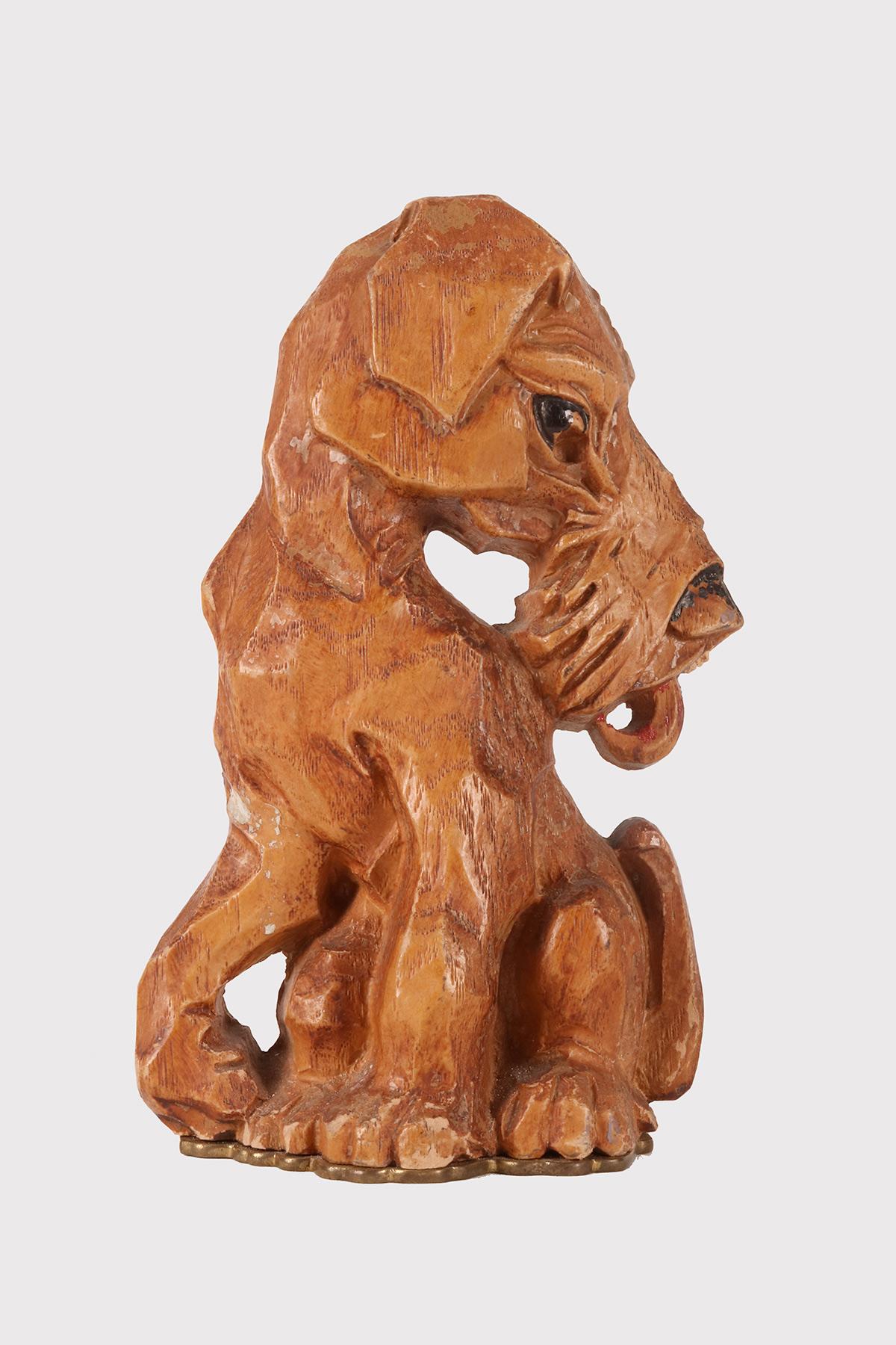 Geschnitzte Buchstütze aus Haselholz, die einen stilisierten Foxterrier in sitzender Position darstellt. Die Augen, die Nase und die Zunge sind mit farbigen Streifen versehen, der Sockel ist aus Messing gefertigt. England, um 1950.