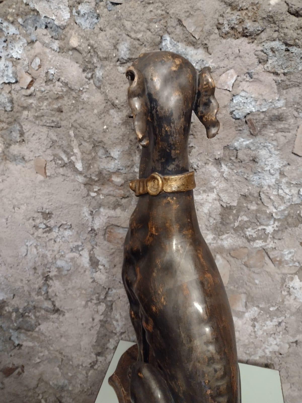 The dog is in gilt  carved wood  We believe to be an Italian greyhound sitting on its haunch. It has a gold buckled dog collar around the neck. The dog attached to cartouche shaped base that shows traces of the original paint.