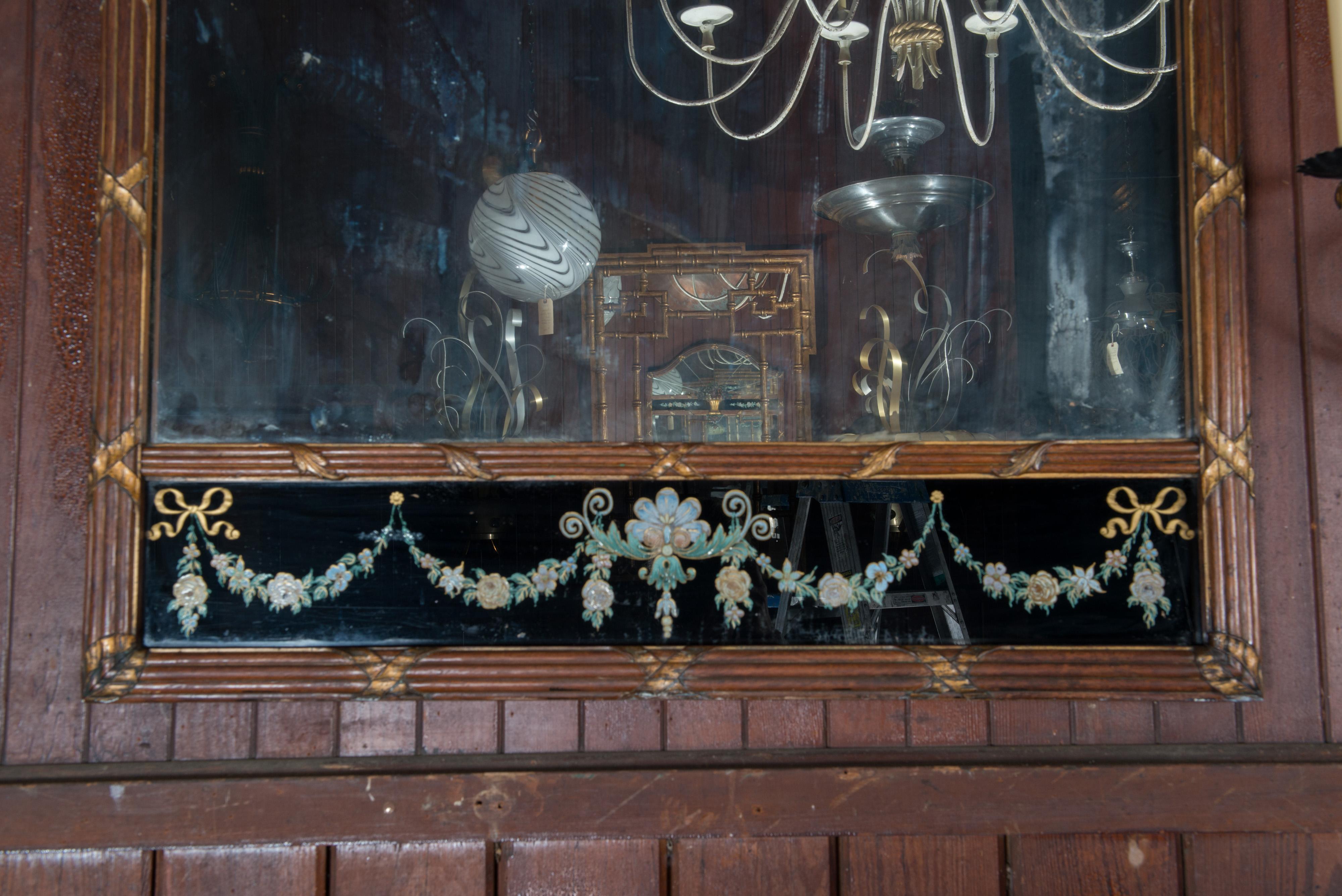 Early 20th century carved wood mirror with striking black background églomisé panels and a basket of flowers. The walnut frame is carved in bundled reed style, with a gentle arch. Old distressed mirror. The small flower below the basket of flowers