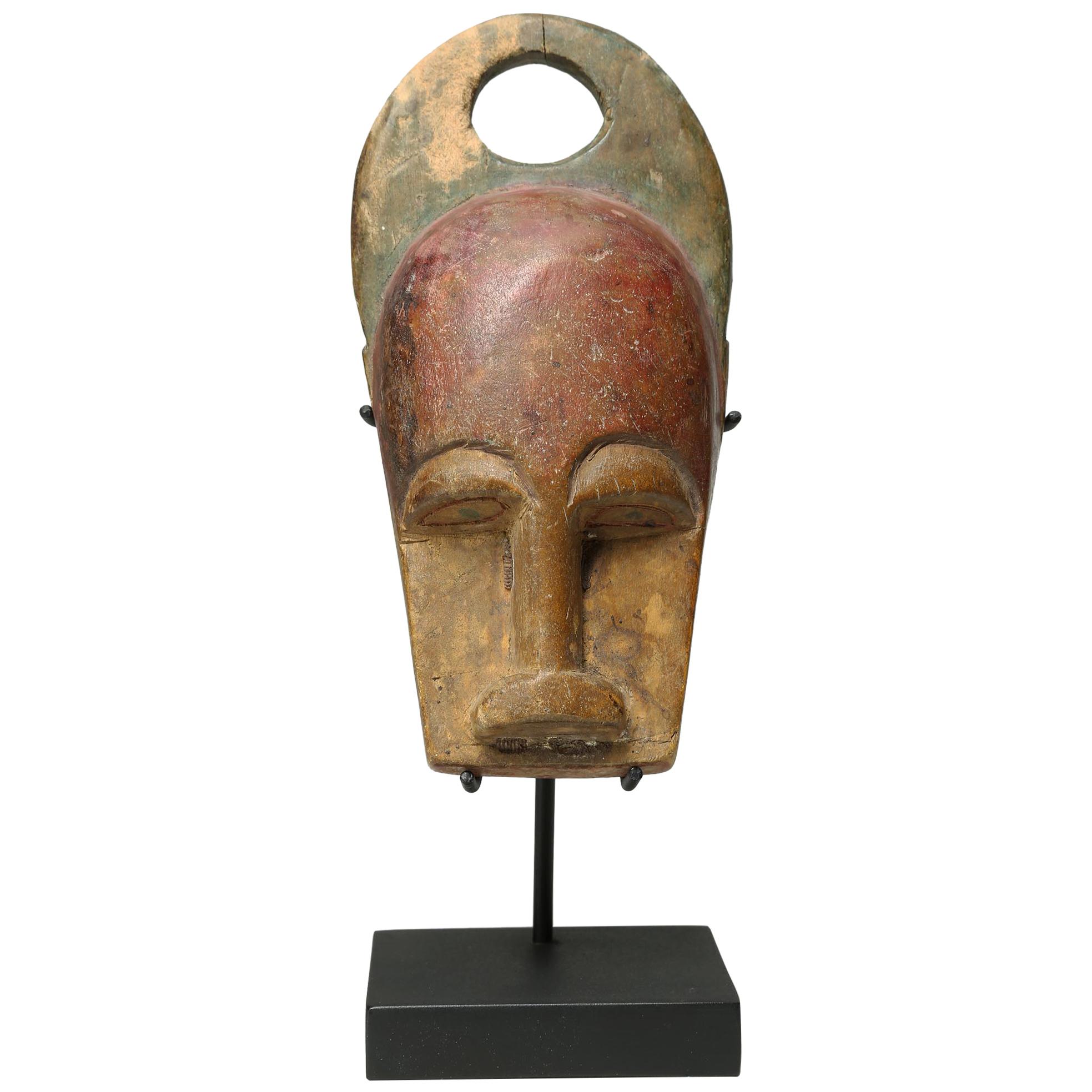 Old carved miniature wood mask with traces of red and green pigment, from the Baule people of Ivory Coast, Africa. Representing a bushcow, and dating from the early 20th century. Mask measures 7 x 3 x 1 3/4 inches. On custom stand as shown 9 inches