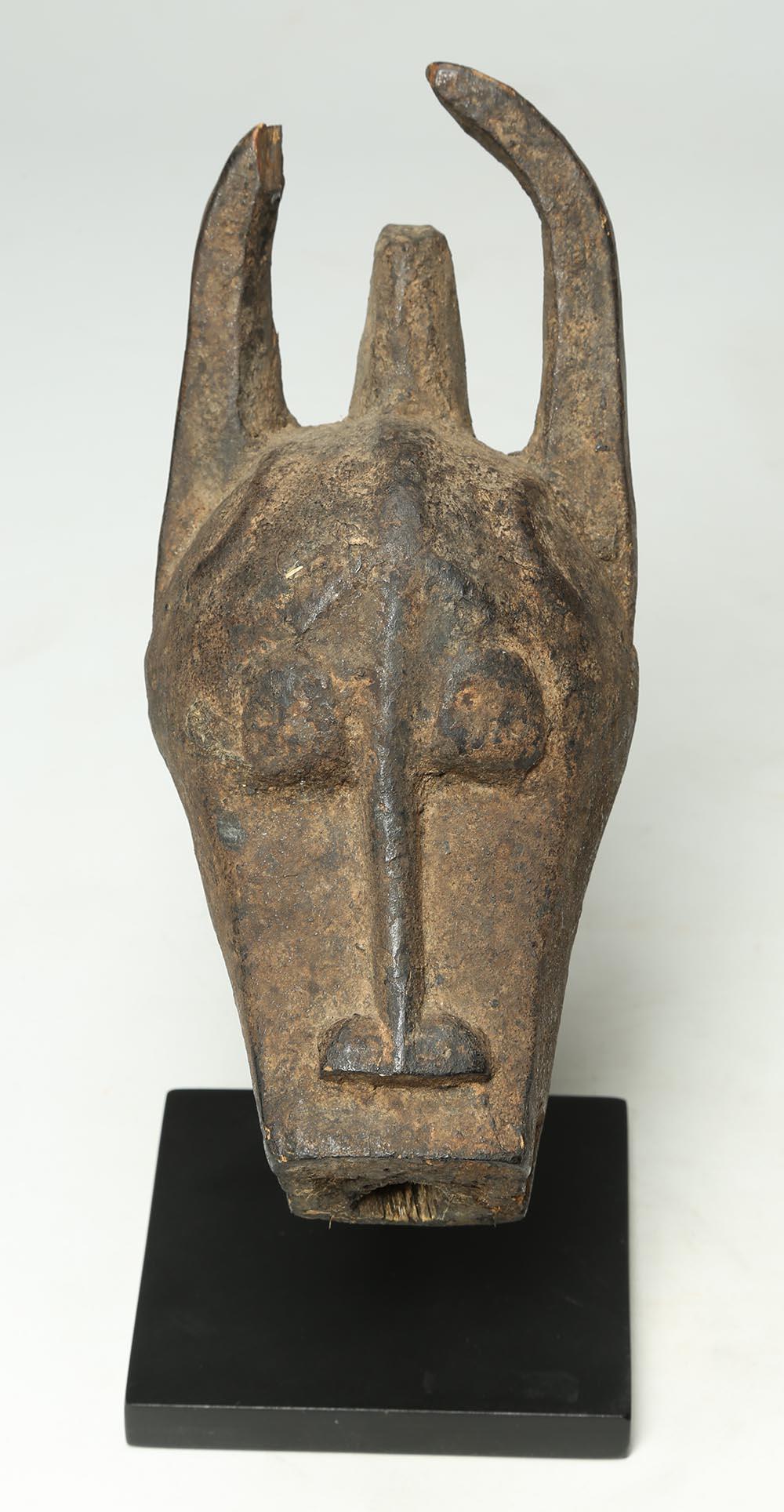 Old carved miniature mask by the Baule of Ivory Coast, West Africa, representing a bushcow with horns (tip of one missing), dark encrusted patina from extensive native use, circular opening on bottom, possibly for attachment to a staff, early 20th