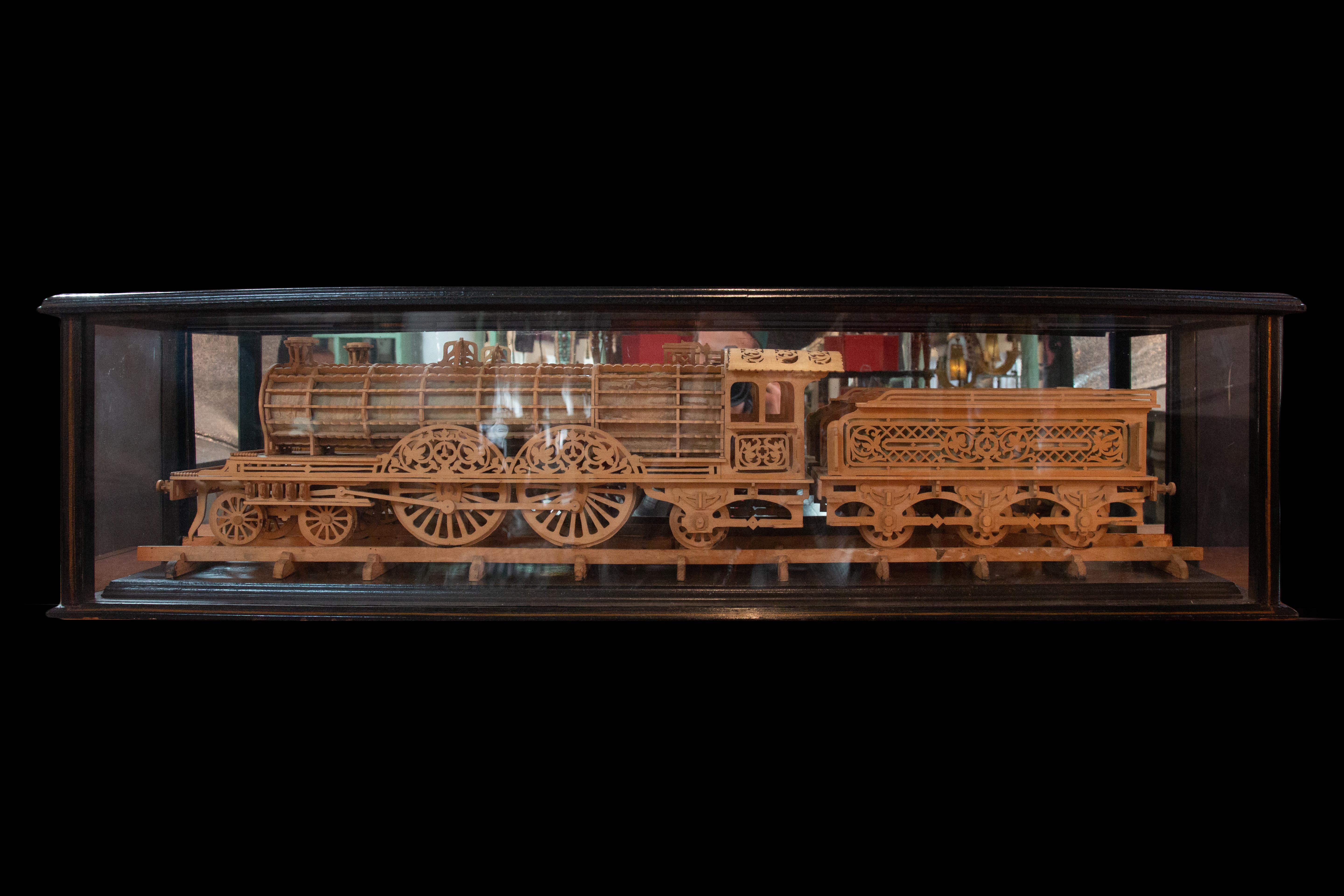 Modèle en bois sculpté d'une locomotive présenté dans un coffret en bois verni et peint. Cette pièce de facture complexe capture l'essence d'une locomotive avec un souci du détail stupéfiant. Le modèle mesure une longueur impressionnante de 42 1/2
