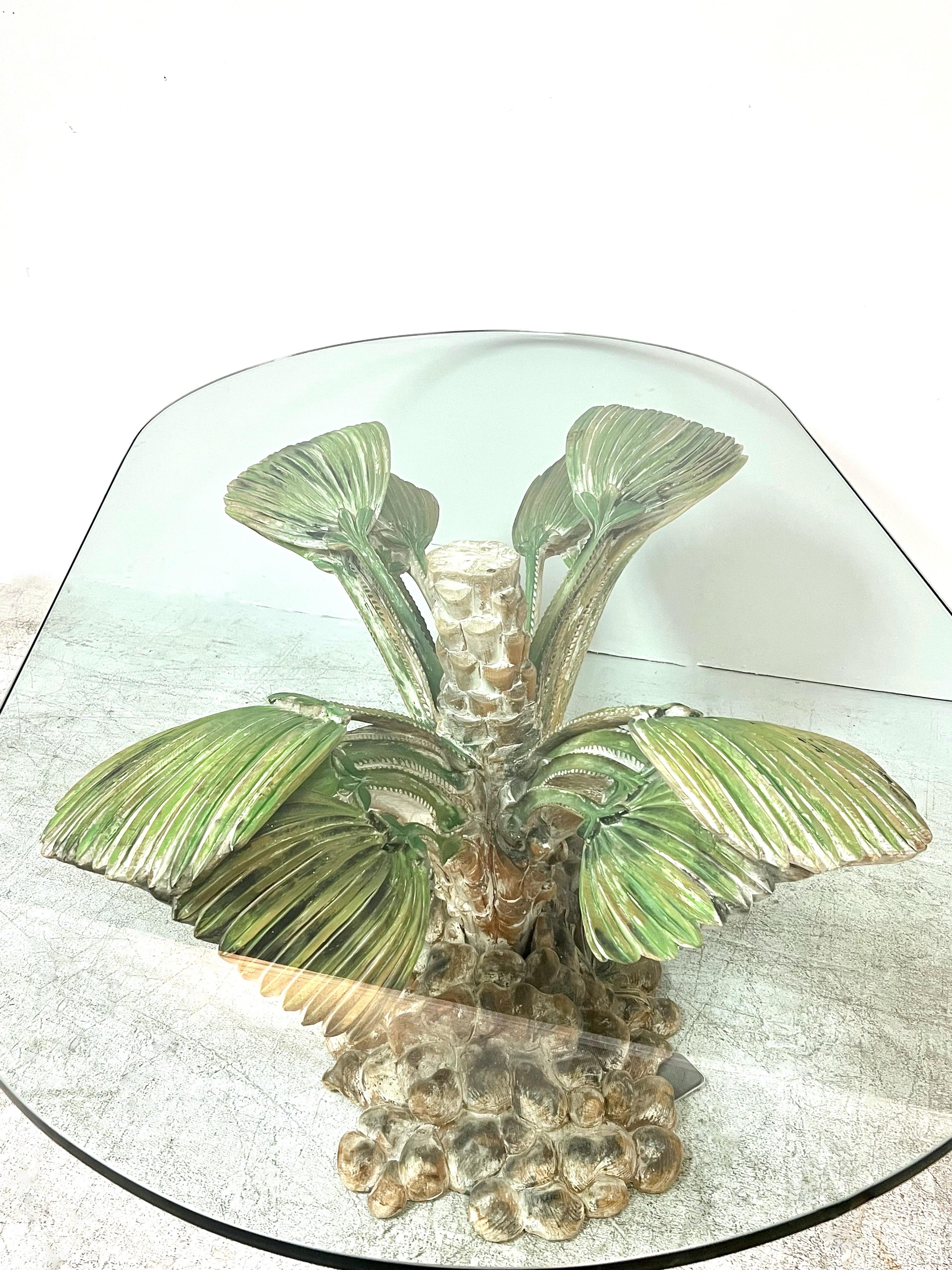 A hand carved sculptural table base in palm tree form. The trunk raises from a bed of rocks and the frond opens to hold the thick glass top. Quite unique.