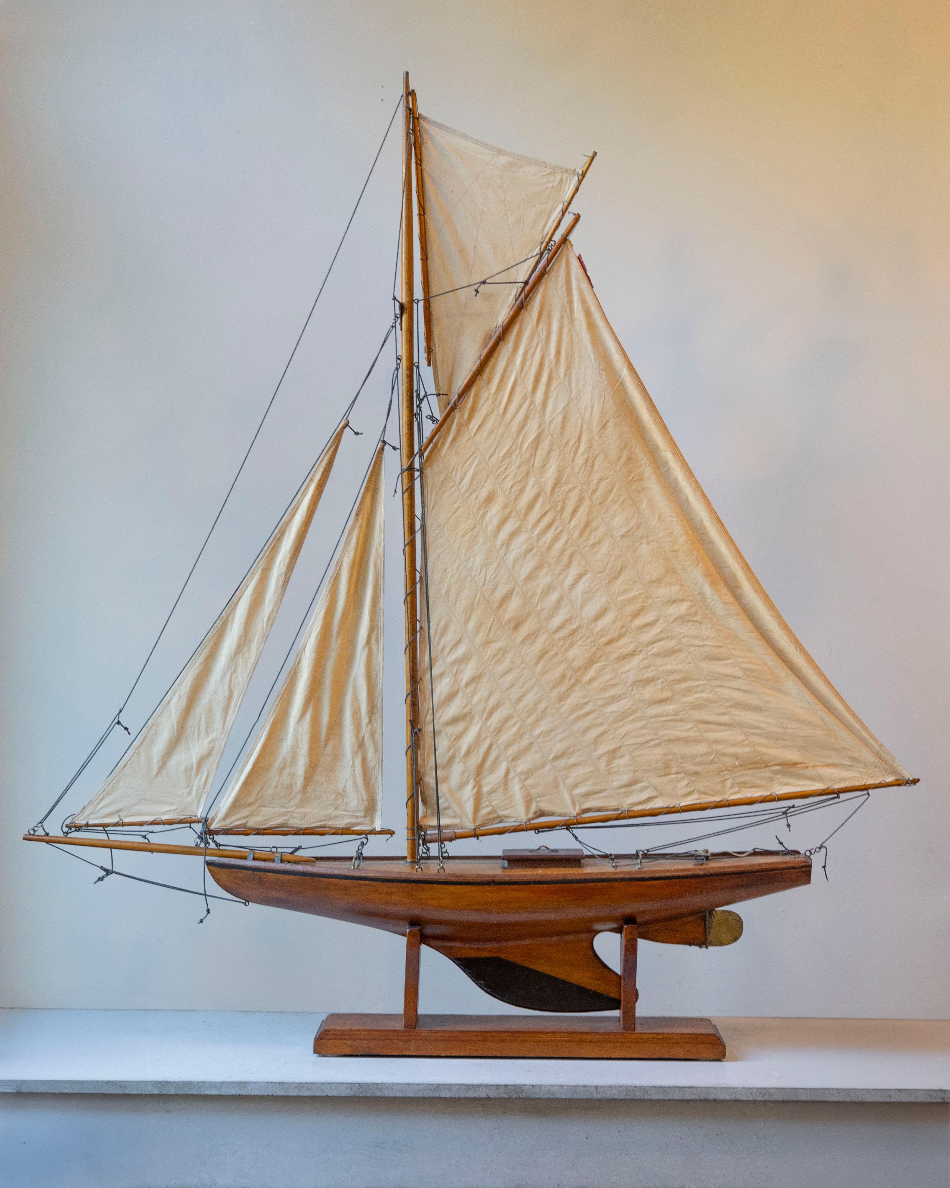 A beautifully carved early 20th-century English model of a racing yawl, featuring an elongated hull in richly varnished wood with graceful overhangs and a classic lead keel. Twin masts are rigged with gaff-rigged cream cotton sails and finely