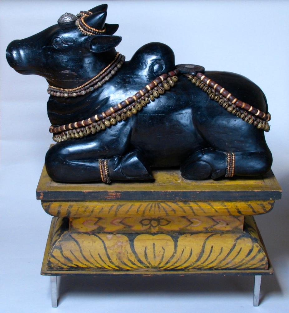 South Indian carved wood sculpture depicting the Hindu Deity of Nandi, a recumbent black bull figure, known within the Hindu faith as the vehicle for Siva, often depicted in sculpture in a Hindu temple facing Lord Siva, and venerated as a