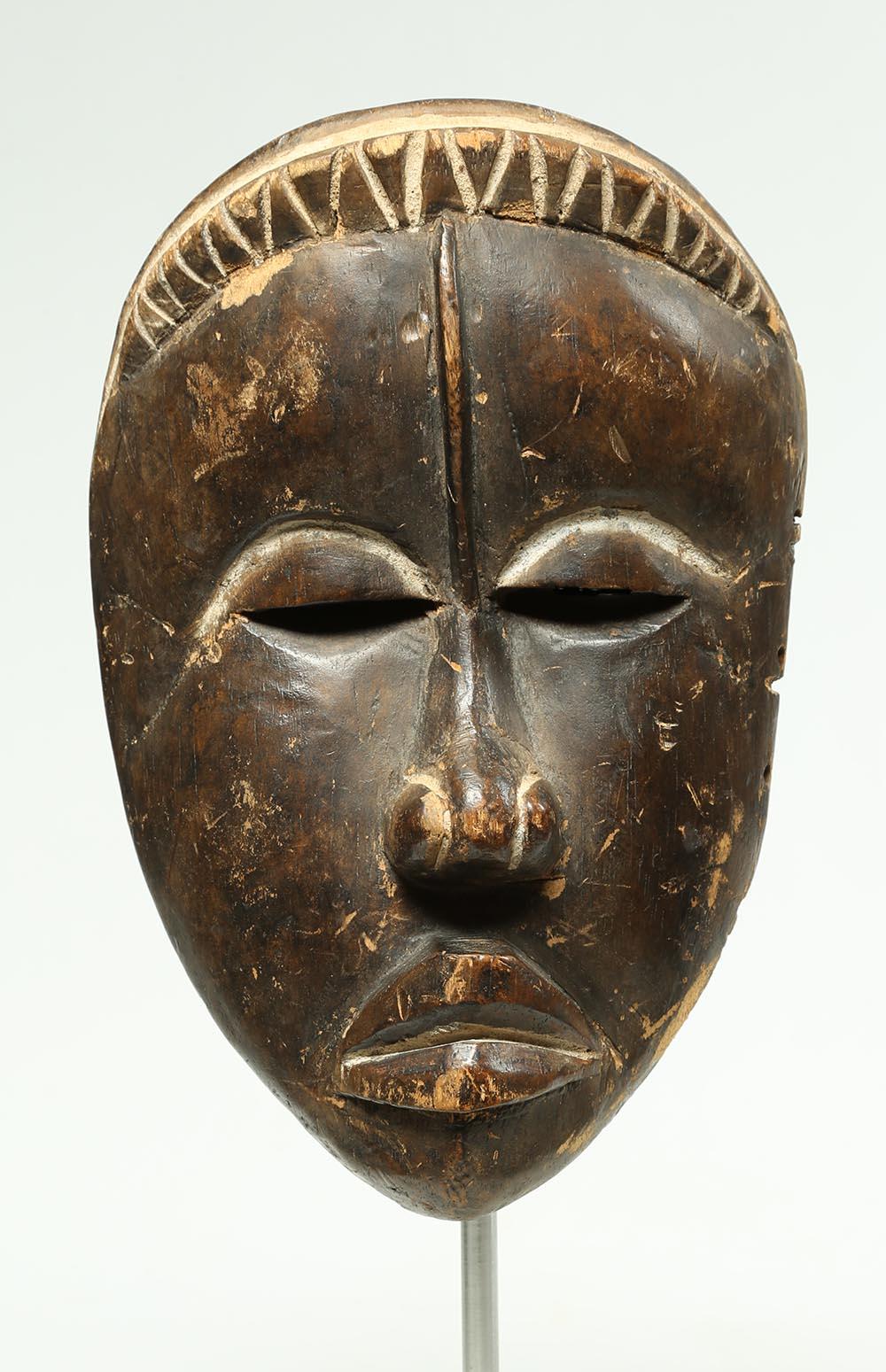 Carved wood tribal Dan mask

Old carved dry oxidized wood Dan mask with a touch of whimsey in its asymmetrical face. Some chips and areas of wear. Traces of white pigments, on custom aluminum base. Mid-20th century. Mask measures: 10 x 6 1/2 x 3