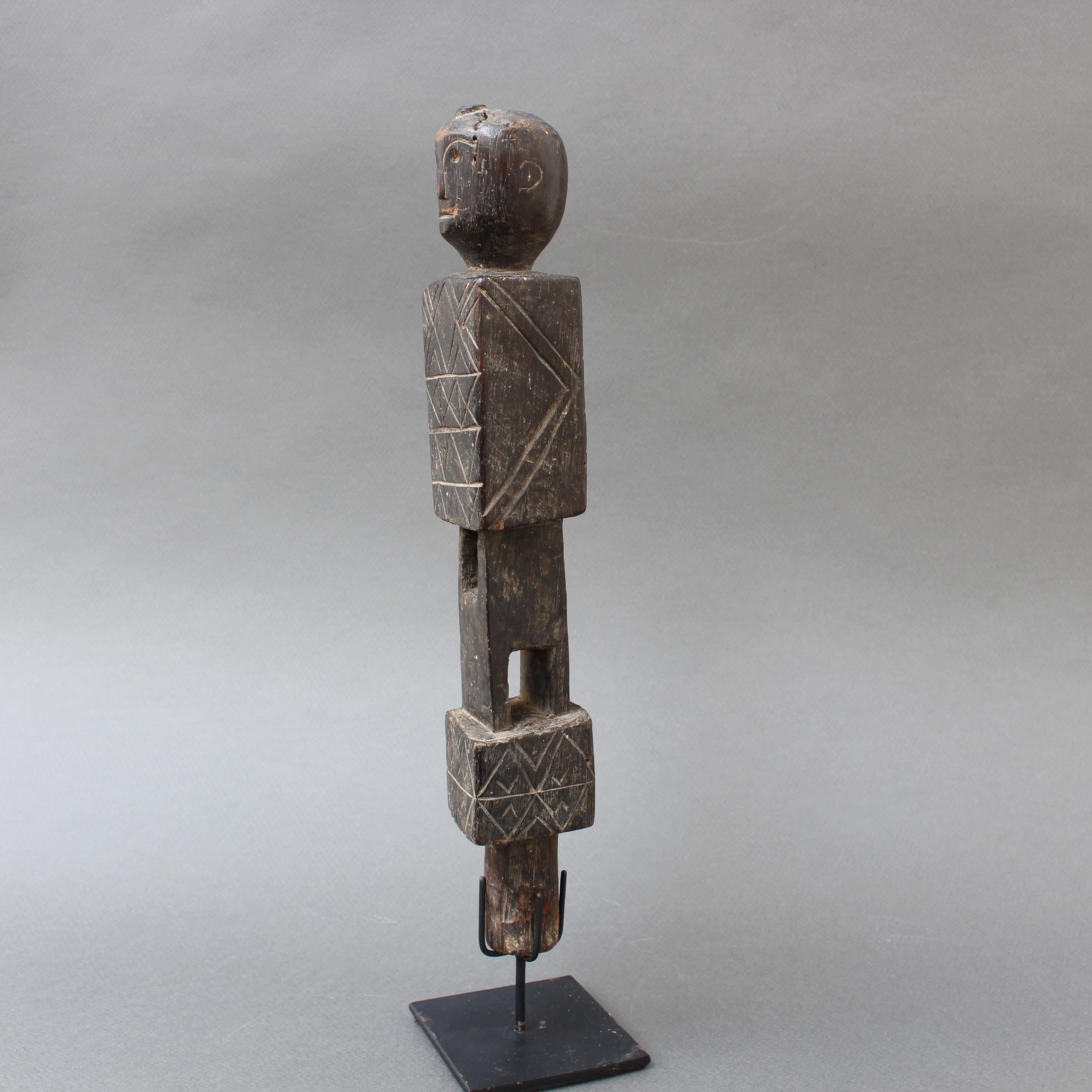 Carved wooden vise tool with human figure finial from Nias, Indonesia (circa 1960s-1970s). A striking carved piece with geometric patterns on the top and bottom of the figure. Rectangular voids are cut into the figure's length most likely so that it