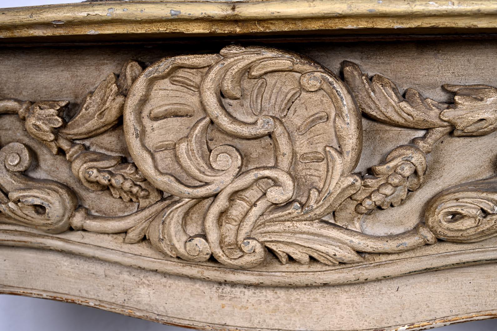Elegante chimenea de madera tallada de finales del siglo XVIII, de abeto y nogal. Su frontón está decorado con una rica decoración tallada de volutas de follaje y un medallón central con motivos estilizados. Los montantes están decorados con putti