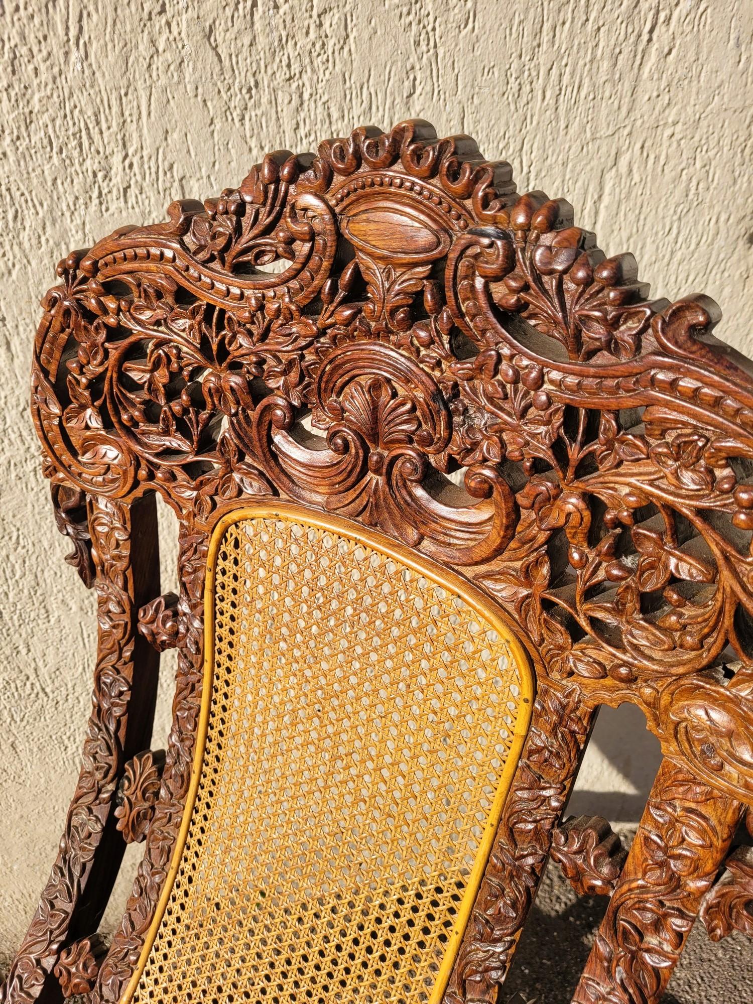 Poltrona pieghevole in legno interamente intagliata con un motivo vegetale, foglie e fiori, e poggiante su 6 gambe a forma di zampe

Lo schienale e la seduta sono rivestiti in canna

Alcuni segni di usura e piccole perdite

Opera indiana,