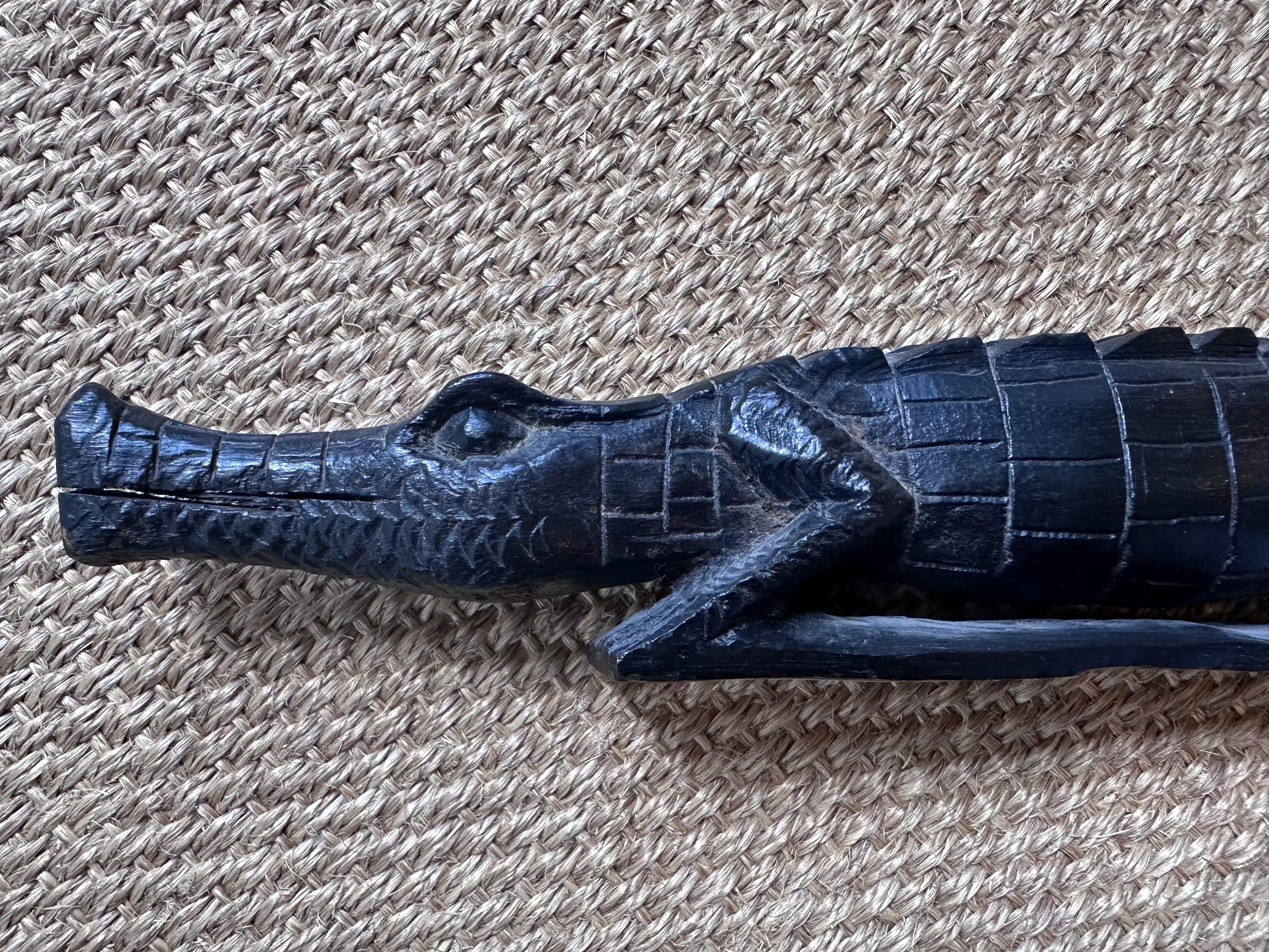 Il s'agit d'une sculpture en bois d'un alligator ou d'un crocodile, réalisée dans un bois teinté foncé. La figure est allongée et stylisée, l'accent étant mis sur la texture et les détails.

Le dos présente un motif méticuleusement sculpté