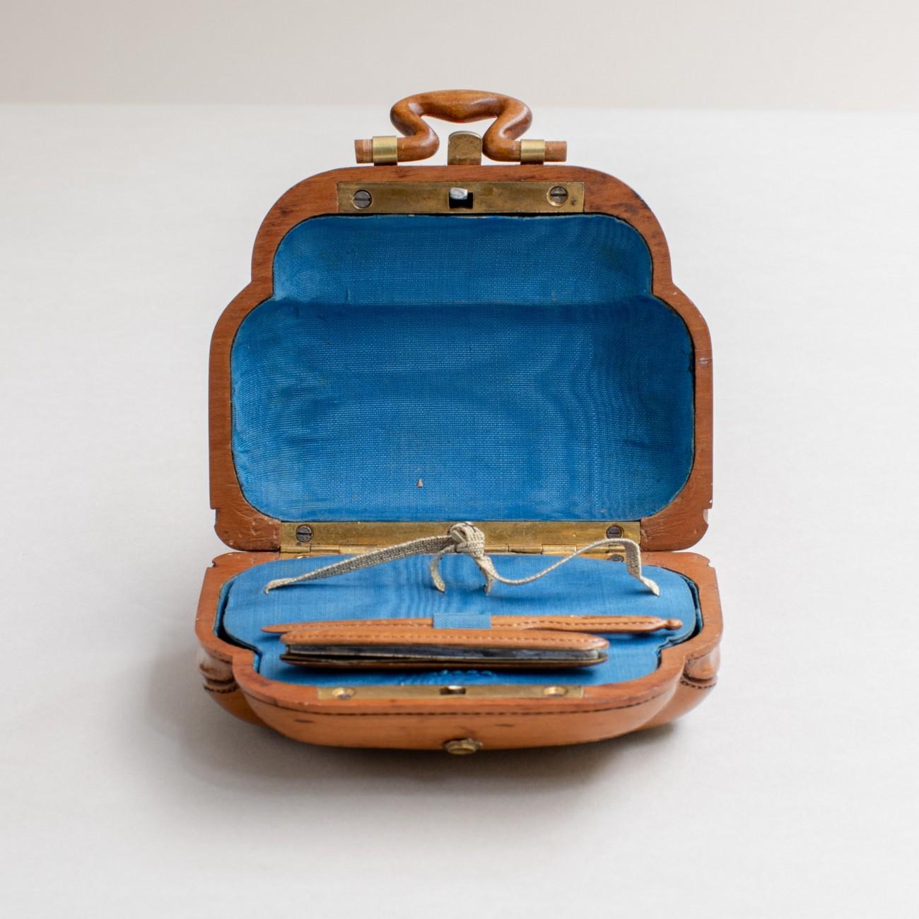 Intricately carved in fruitwood, modelled as a miniature leather travel bag, circa 1900. The interior has the original blue silk lining. This spectacular miniature was originally made as a sewing kit.

Dimensions: 9 cm/3½ inches (length) x 4 cm/1½