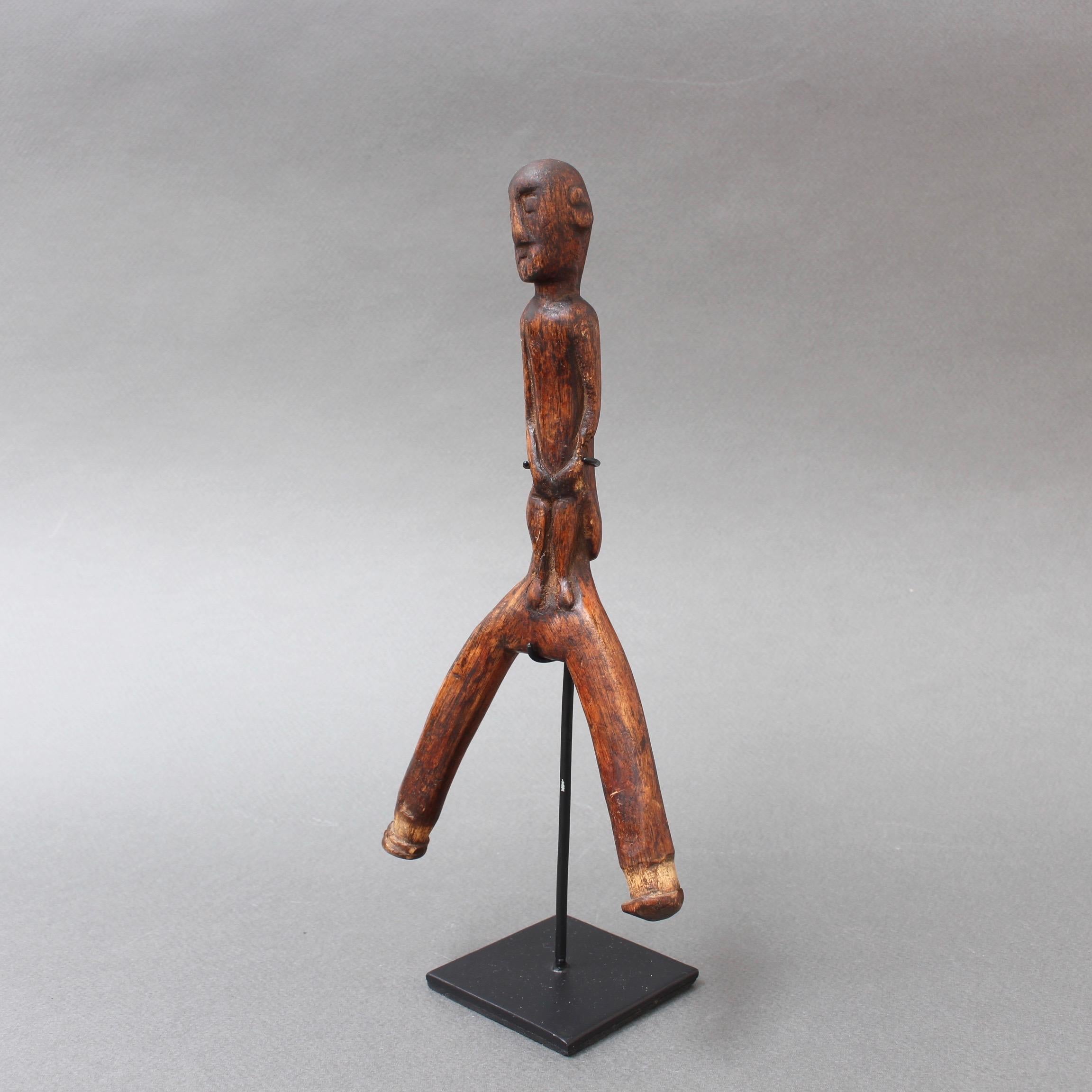 Carved wooden slingshot figure from Timor Island, Indonesia (circa 1970s) on contemporary stand. The standing figure forms the handle of this tribal weapon used to fire projectiles, perhaps at small game or for sport. Human figures were often carved