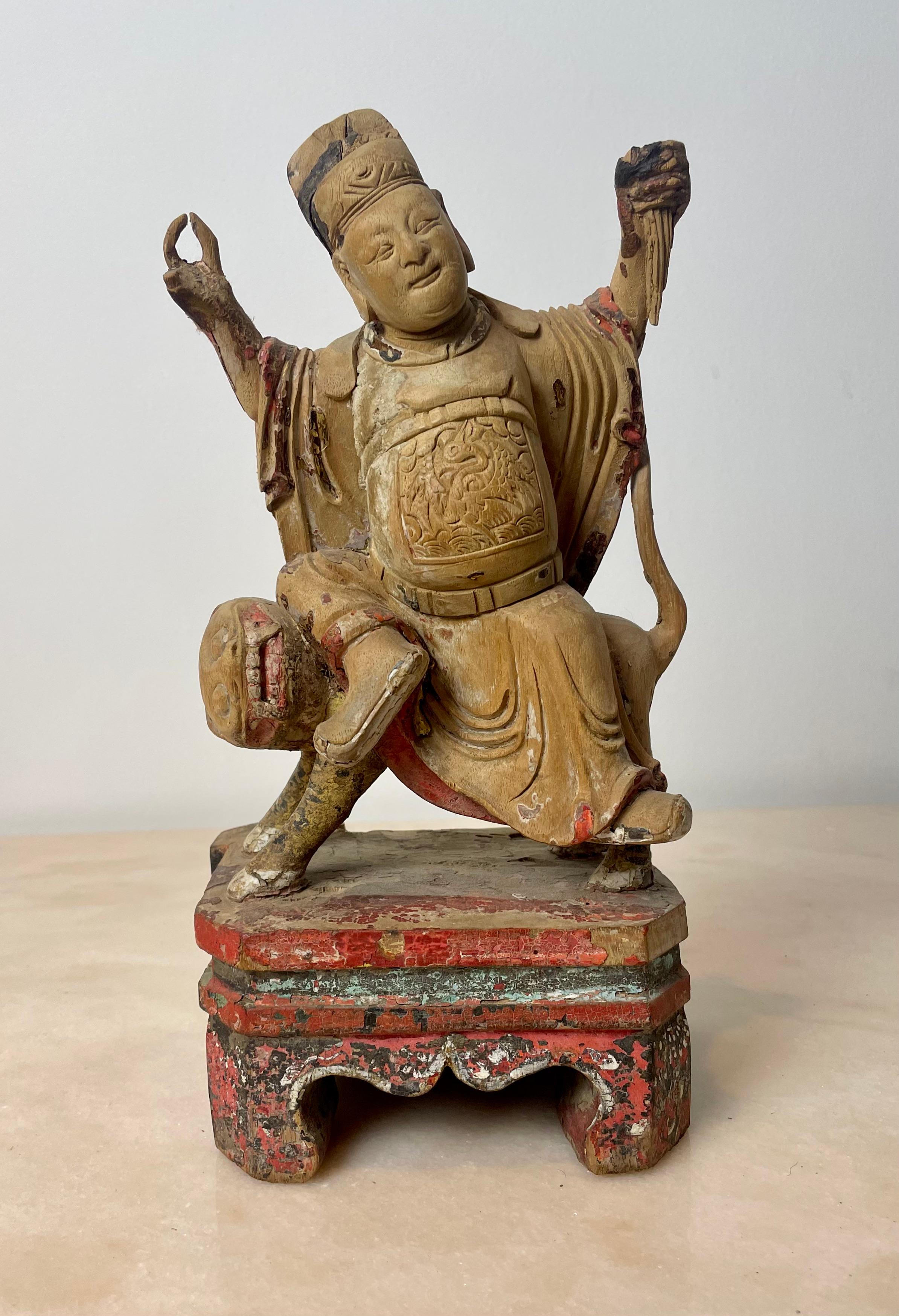 This marvelous polychrome carved wooden statuette represents a Buddhist temple guardian, Guandi or Guan Yu sitting on a Fo dog.
The guardian and the dog are on a base whose feet recall the shape of the temples.
The temple guardian has a peaceful and