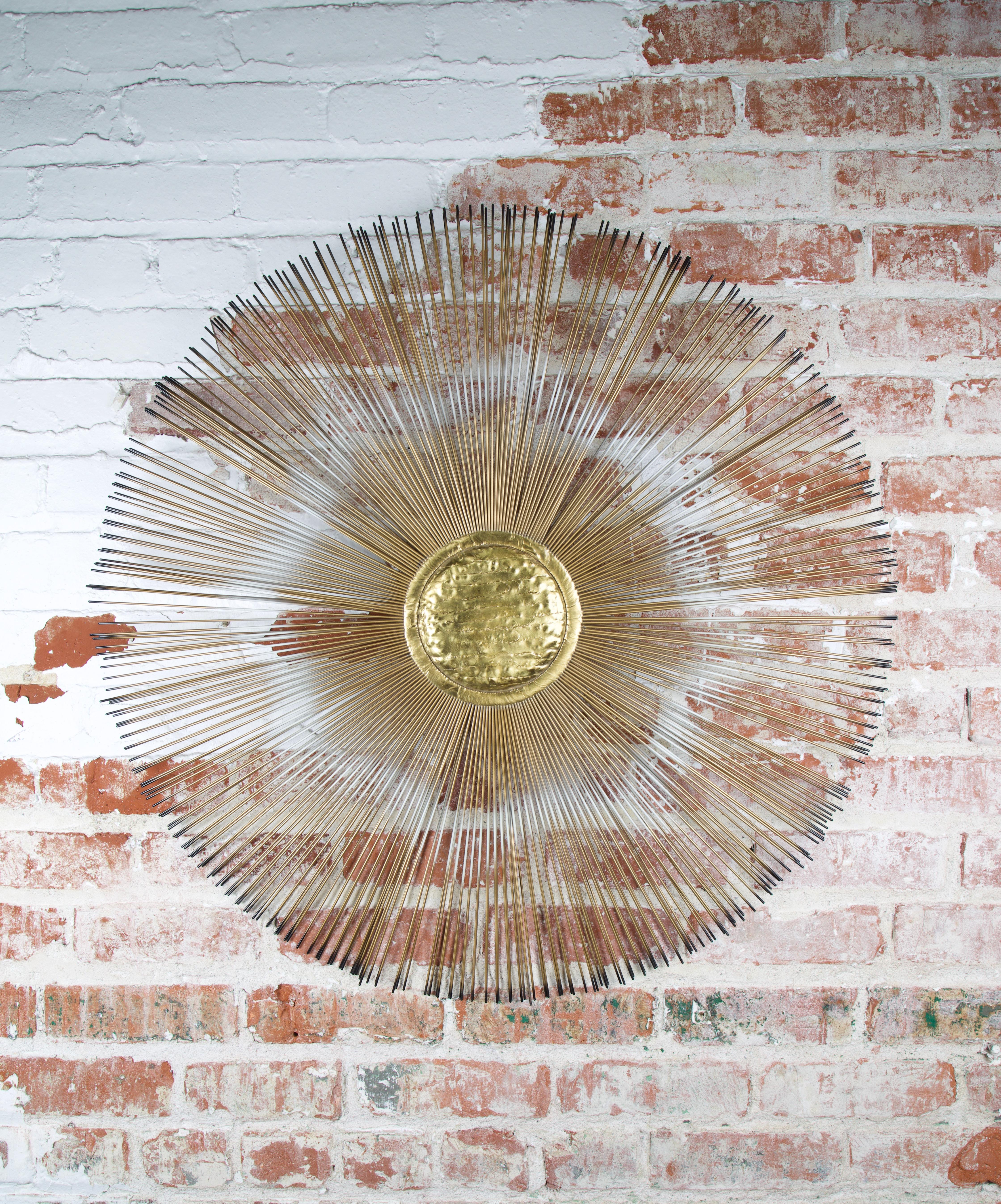 Sunburst wall sculpture with a hammered brass center and two layers of painted rods creating a sunburst effect. The artist hand signed the sculpture on the verso.