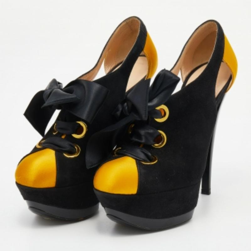 Crea una silueta impresionante con este par de botines de Casadei. Confeccionados en ante negro y satén amarillo, los zapatos se estilizan con cordones, detalles recortados y se elevan sobre altas plataformas y tacones de 14 cm.