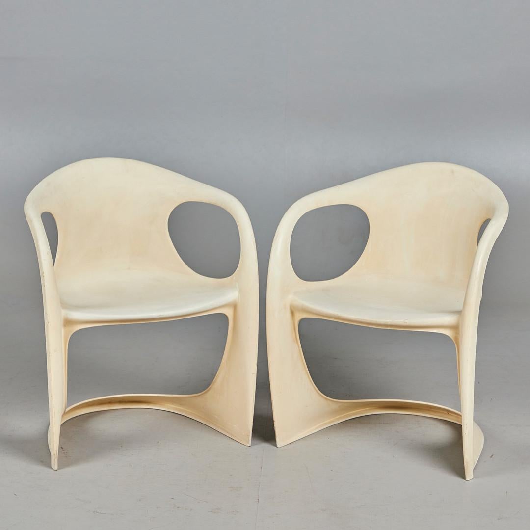 The chair is formed in an organically shaped frame made of eggshell-coloured plastic with armrests, embossed with the manufacturer on the underside.
  