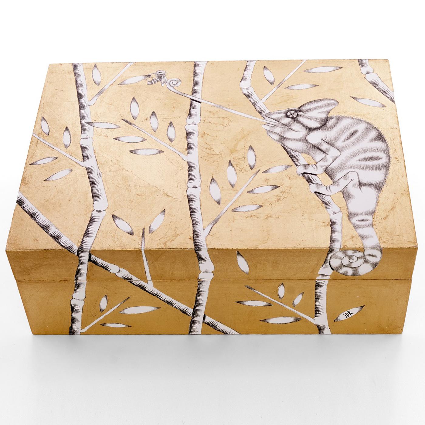 Hand-made box with gold leaf application on graphite drawing. A chameleon climbs up from the paper to the branches around the wooden box. Entirely decorated by hand with gold leaf on the print of an original graphite drawing. Finished with shellac.