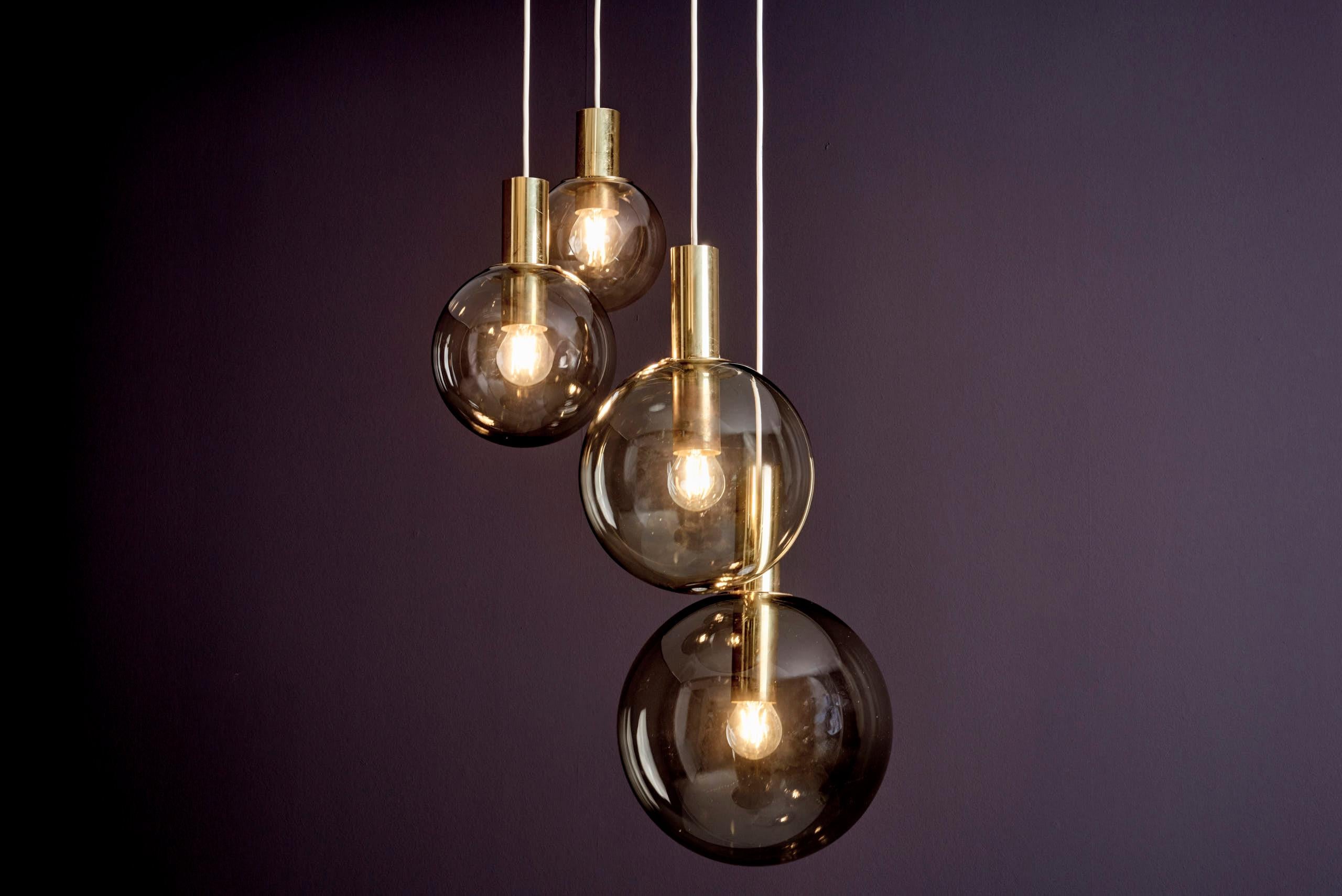 Mid-Century Modern cascade pendant by Glashütte Limburg, Germany, 1970s.
This elegant fixture features four smoked, hand-blown glass globes suspended at staggered heights from a white metal ceiling plate that conceals the wiring. Brass bulb holders