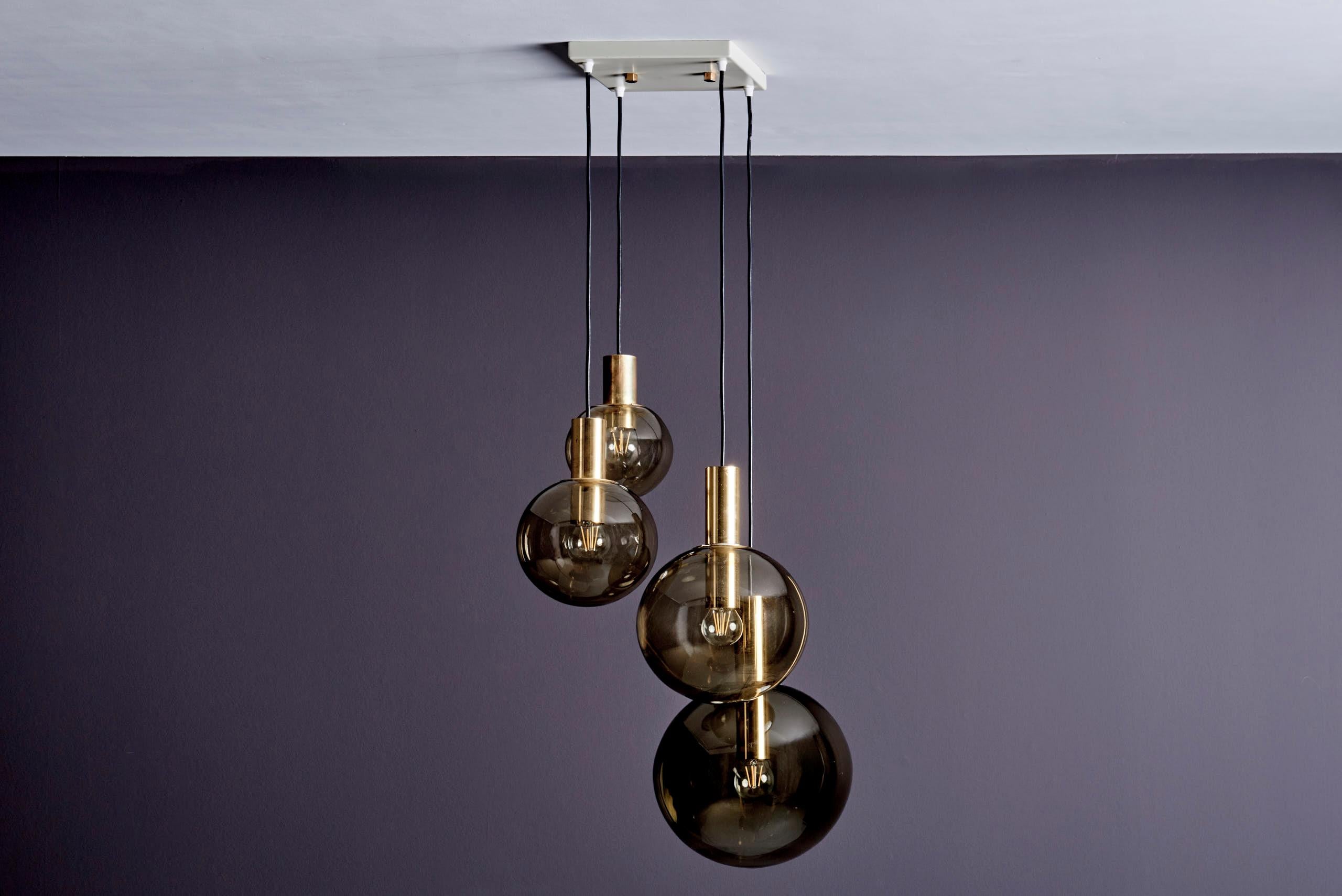 Mid-Century Modern cascade pendant by Glashütte Limburg, Germany, 1970s.
This elegant fixture features four smoked, hand-blown glass globes suspended at staggered heights from a white metal ceiling plate that conceals the wiring. Brass bulb holders