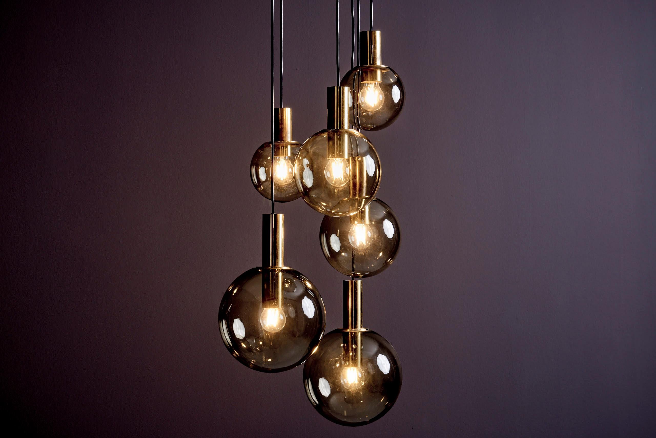 Mid-Century Modern cascade pendant by Glashütte Limburg, Germany, 1970s.
This elegant fixture features six smoked, hand-blown glass globes suspended at staggered heights from a white metal ceiling plate that conceals the wiring. Brass bulb holders
