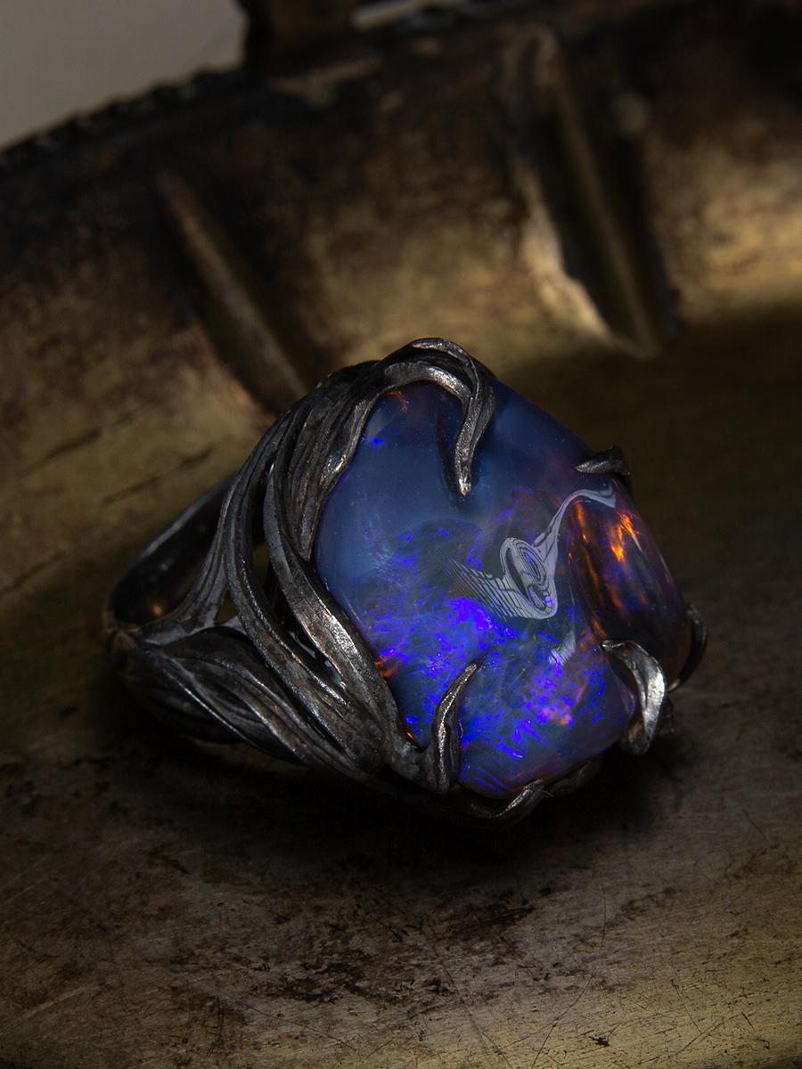 Cascading Waves Natural Dark Neon Electric Opal Ring

Inspired by the sun as it breaks through the dark night, this magnificent ring features fantastical blackened silver waves painstakingly created by hand. An Australian neon blue opal sits in the