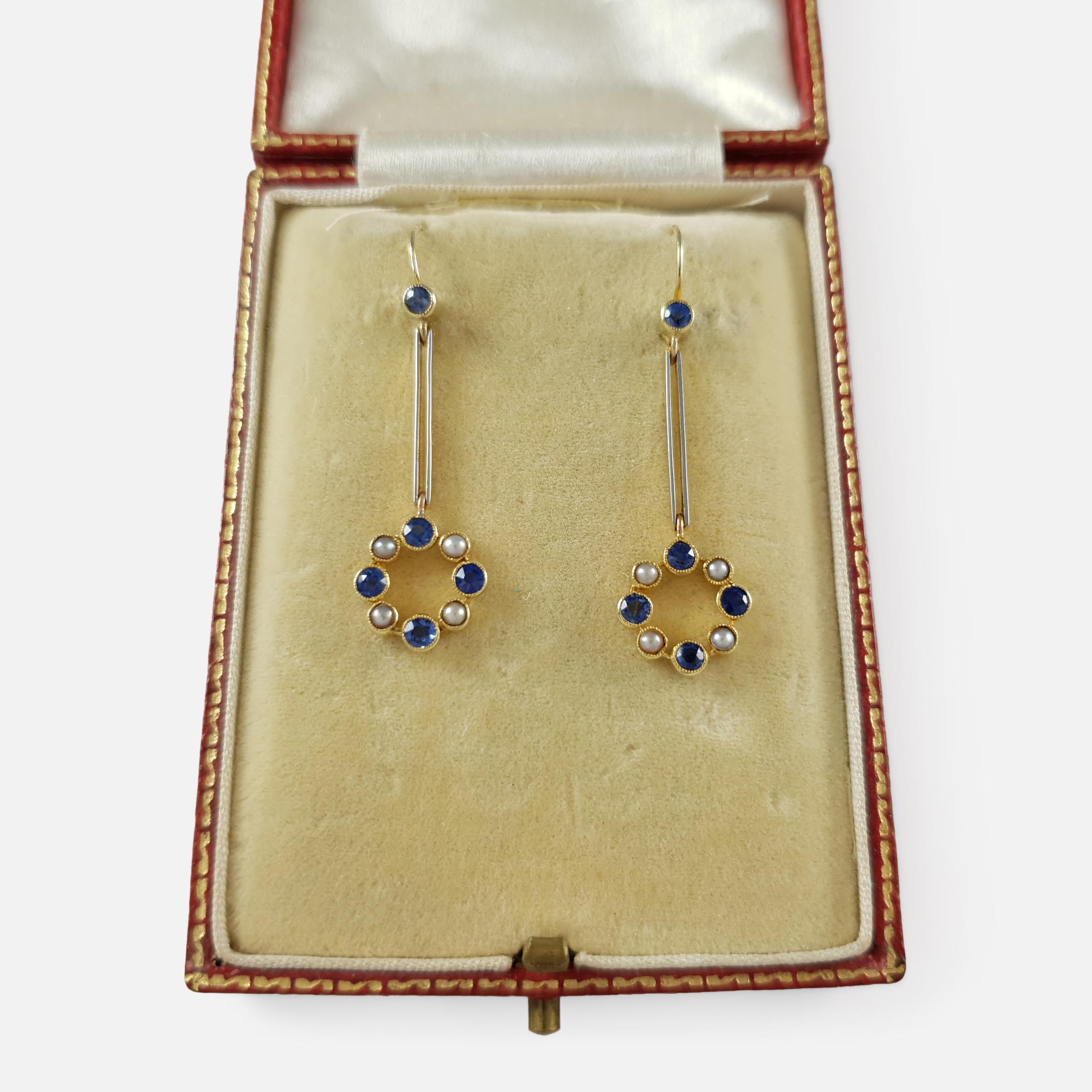 Description: - This is a stunning pair of cased 15 karat gold sapphire and seed pearl pendant drop earrings. The earrings are set with a single sapphire, that suspends a bar leading to a further halo set with four sapphires and four seed pearls. 