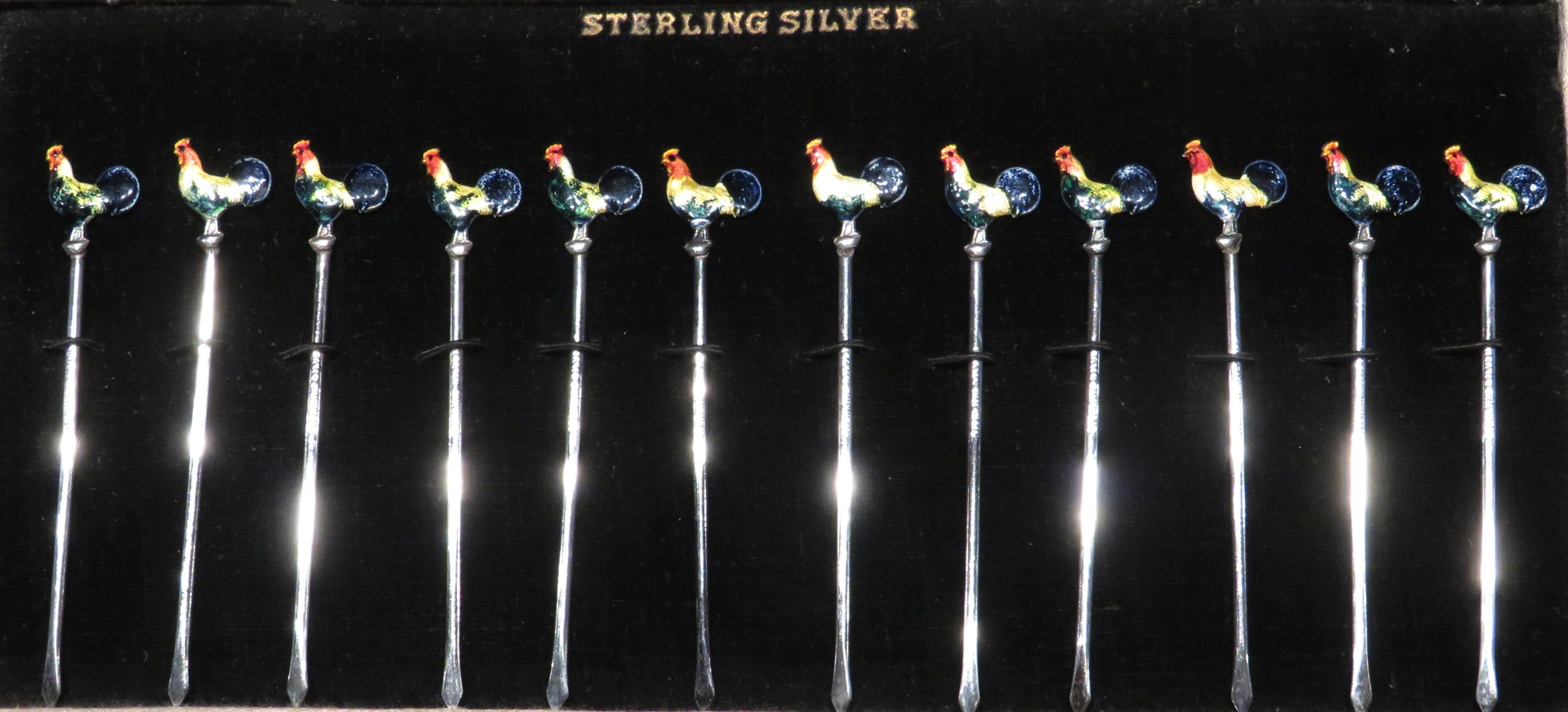 A very charming & festive set of 12 sterling silver Art Deco cocktail picks, all showing finials in the form of cockerels decorated by hand with brilliant multi-coloured enamels. All are stamped sterling silver and set within their original velvet