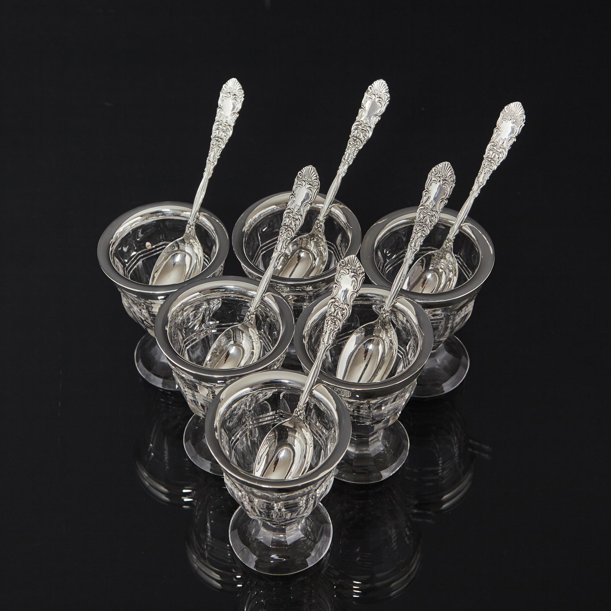 Quite a rare set of collected Edwardian cut glass egg cups with silver rims and a set of decorative spoons. The glass egg cups are cut with panels and feature a horizontal thread pattern around the bodies. The rims are sterling silver and the