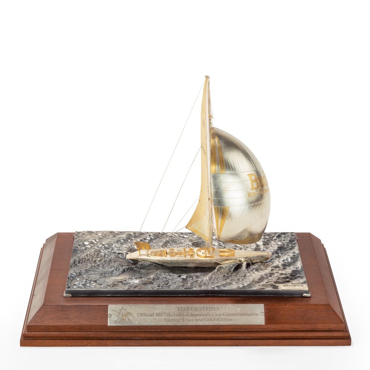 A cased silver and gilt model of 12 meter America’s Cup yacht Stars & Stripes 87, the yacht shown sailing under spinnaker. The mainsail with the numbers 12 US 55 the spinnaker with the legend ‘BUD King of Beers’. Hallmarked and signed Sterlinghall.
