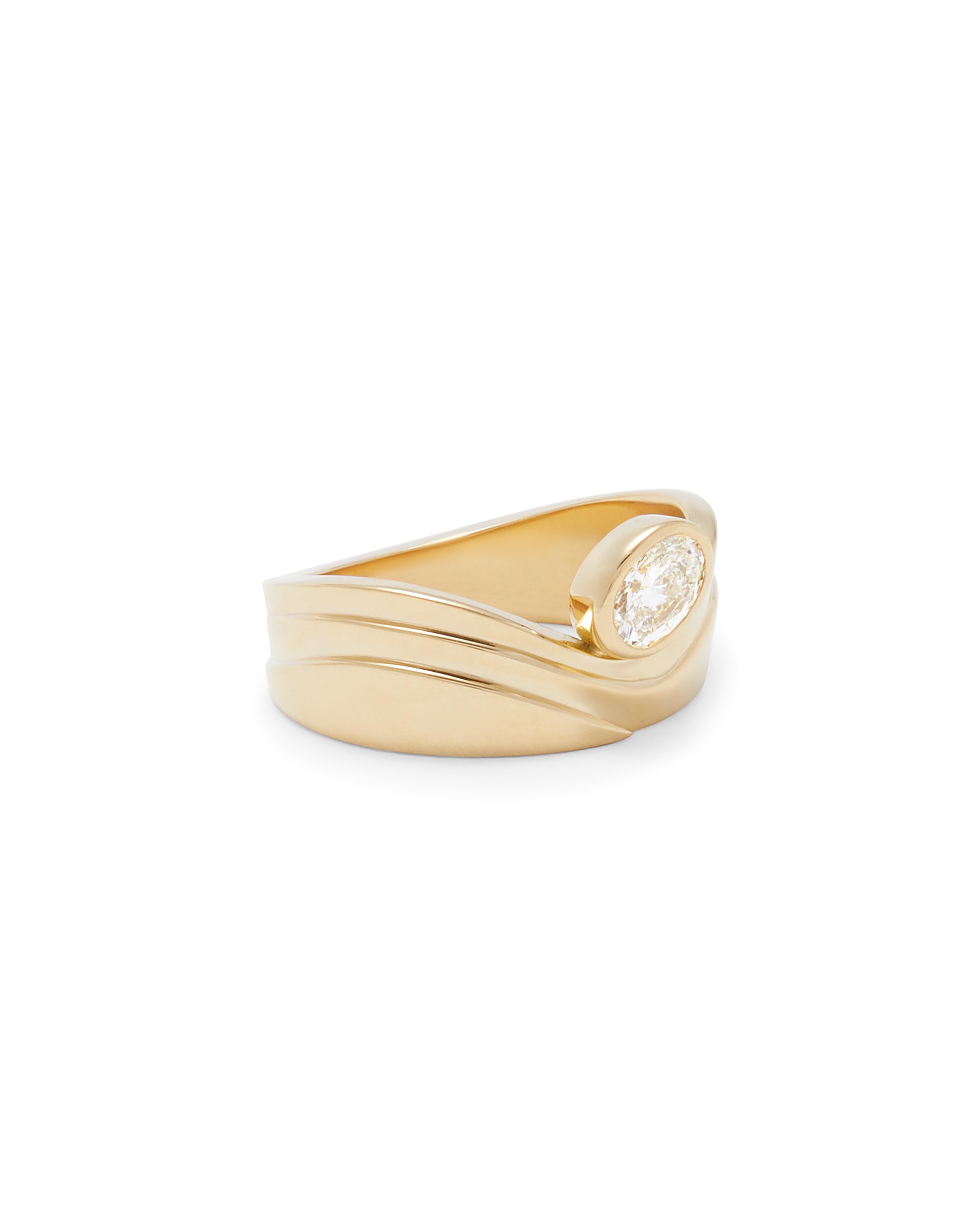 This sculptural gold ring made is made from 18k yellow gold and features a modern tiered design on the band. The flowing curved designed is accentuated with a bezel set .5 carat brilliant cut oval diamond. The stone shape and size can be customized. 