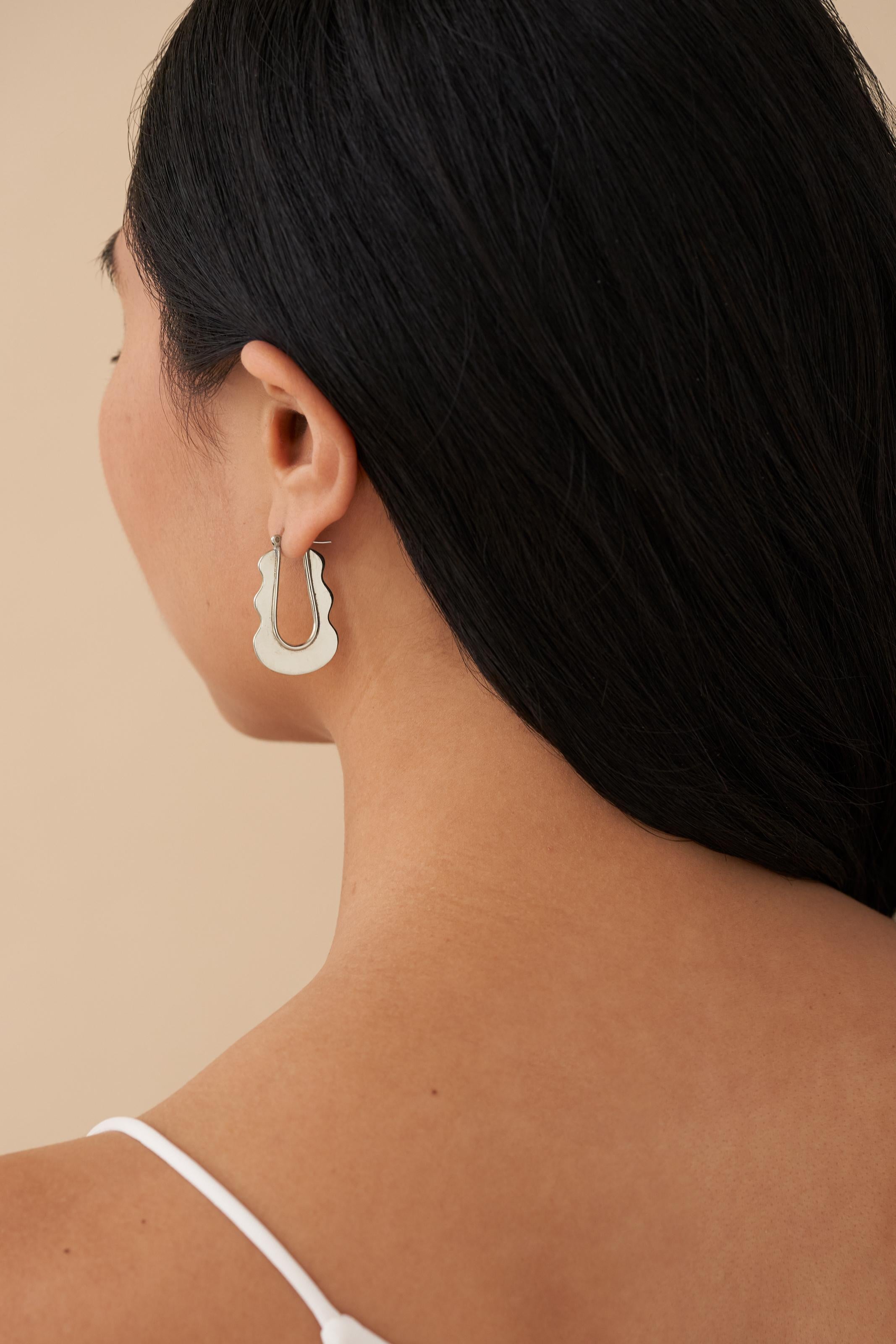 Seeking a subtle statement? Look no further. Our scaled-down version of the Mirage Hoops are the perfect fit. Inspired by Ettore Sottsass’ renowned Ultrafragola mirror, these elegantly undulating hoops add a distinctive touch to any ensemble.