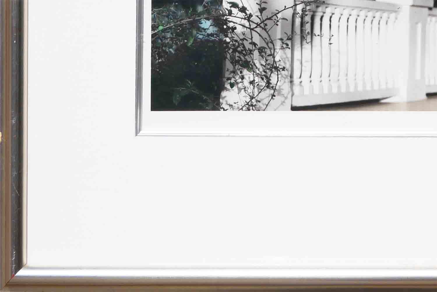 Kontrastreiche zeitgenössische Fotografie des Fotografen Casey Williams aus Houston, TX. Dieses Foto zeigt einen Schnappschuss eines Balkons oder einer Terrasse mit weißem Holzgeländer und Pfosten. Die Farben auf den Fotos lassen vermuten, dass sie