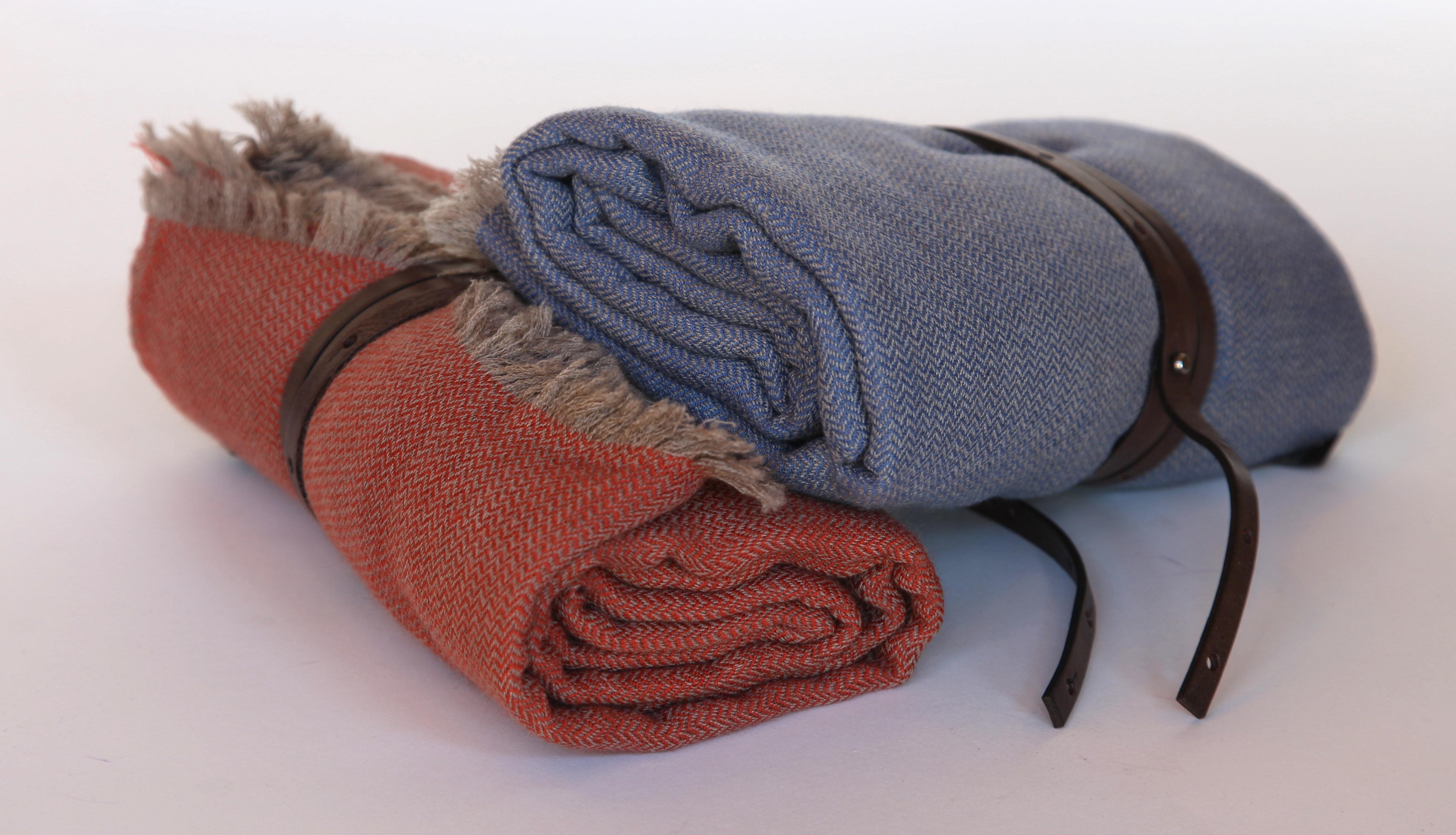 Cashmere travel throw in herringbone pattern with fringe and leather strap. In coral or denim.