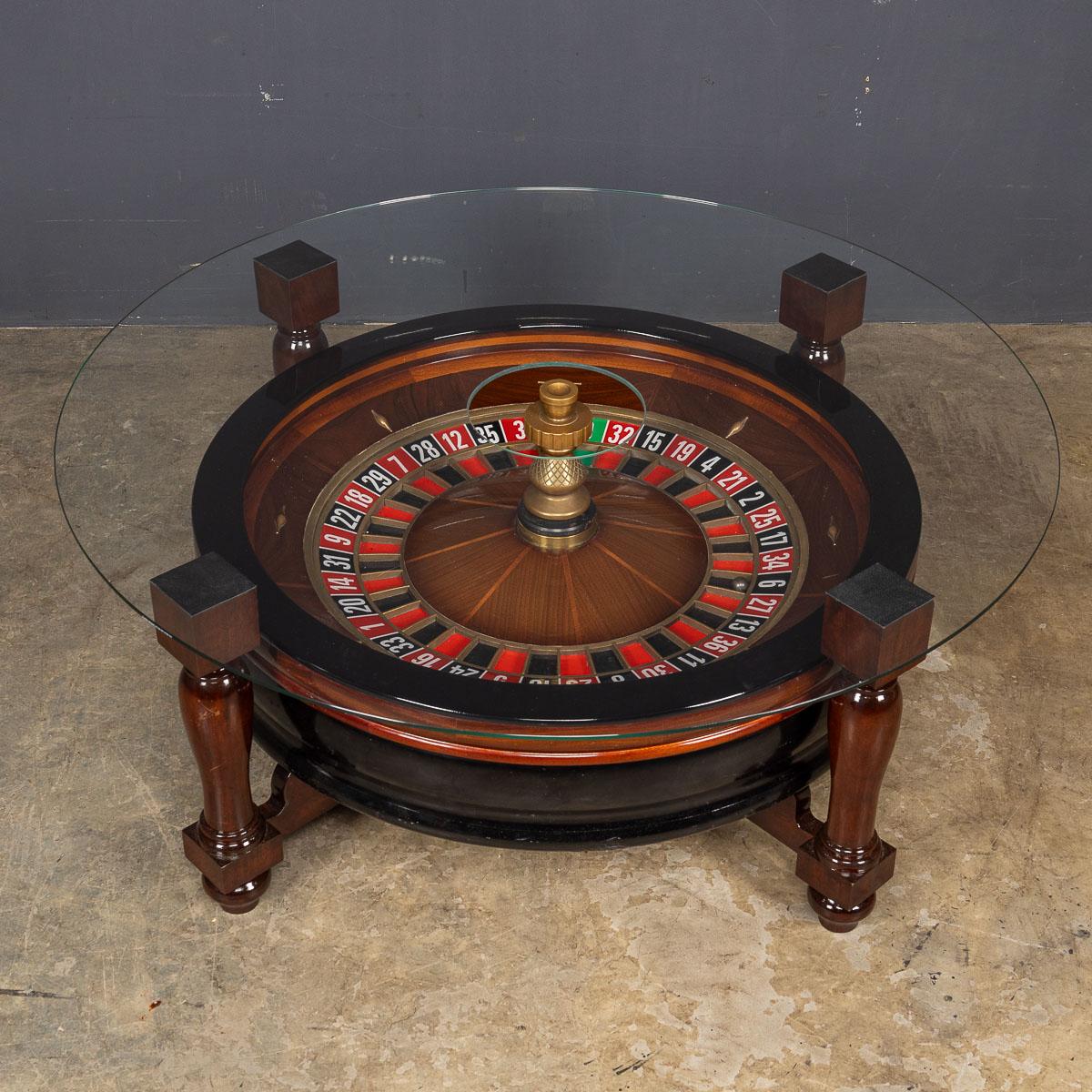 Behold, an exquisite casino roulette wheel, a masterpiece of craftsmanship, resplendent in mahogany wood adorned with intricate brass detailing. This opulent creation rests upon a finely turned mahogany base, elevating it to a true work of art. What