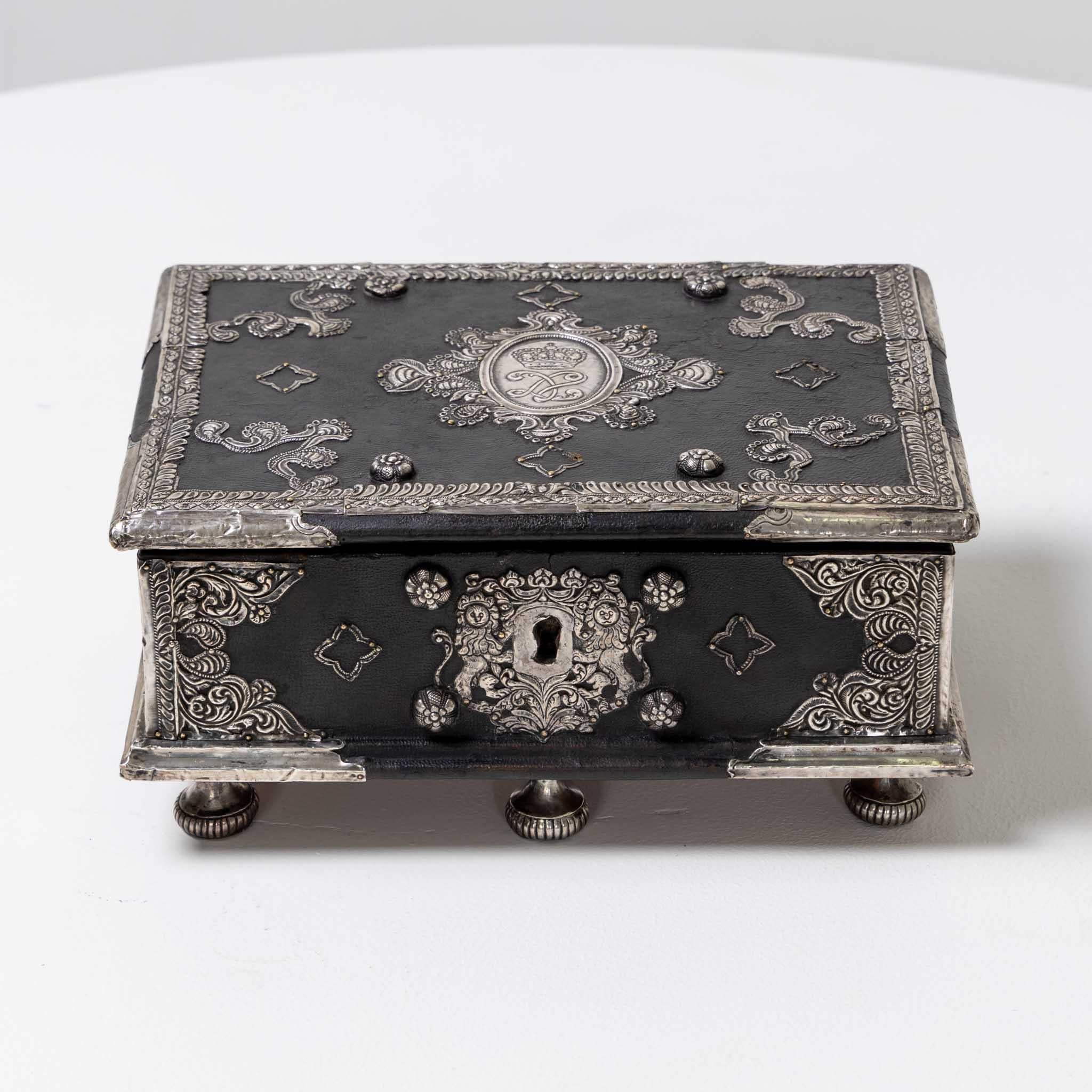 Small Indian lidded casket made of sandalwood. The chest is covered in leather and decorated with silver fittings with handles on the sides. The interior is lined in red velvet. Key present.