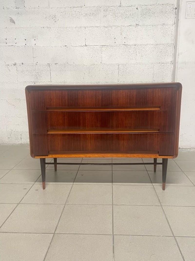 Cassettiera anni '50 a tre cassetti dalle linee morbide.

Lastronatura in legno di palissandro e particolari in mogano biondo.

I tre ampi cassetti non hanno maniglie ma un invito per l'apertura questo denota il design contemporaneo di questo