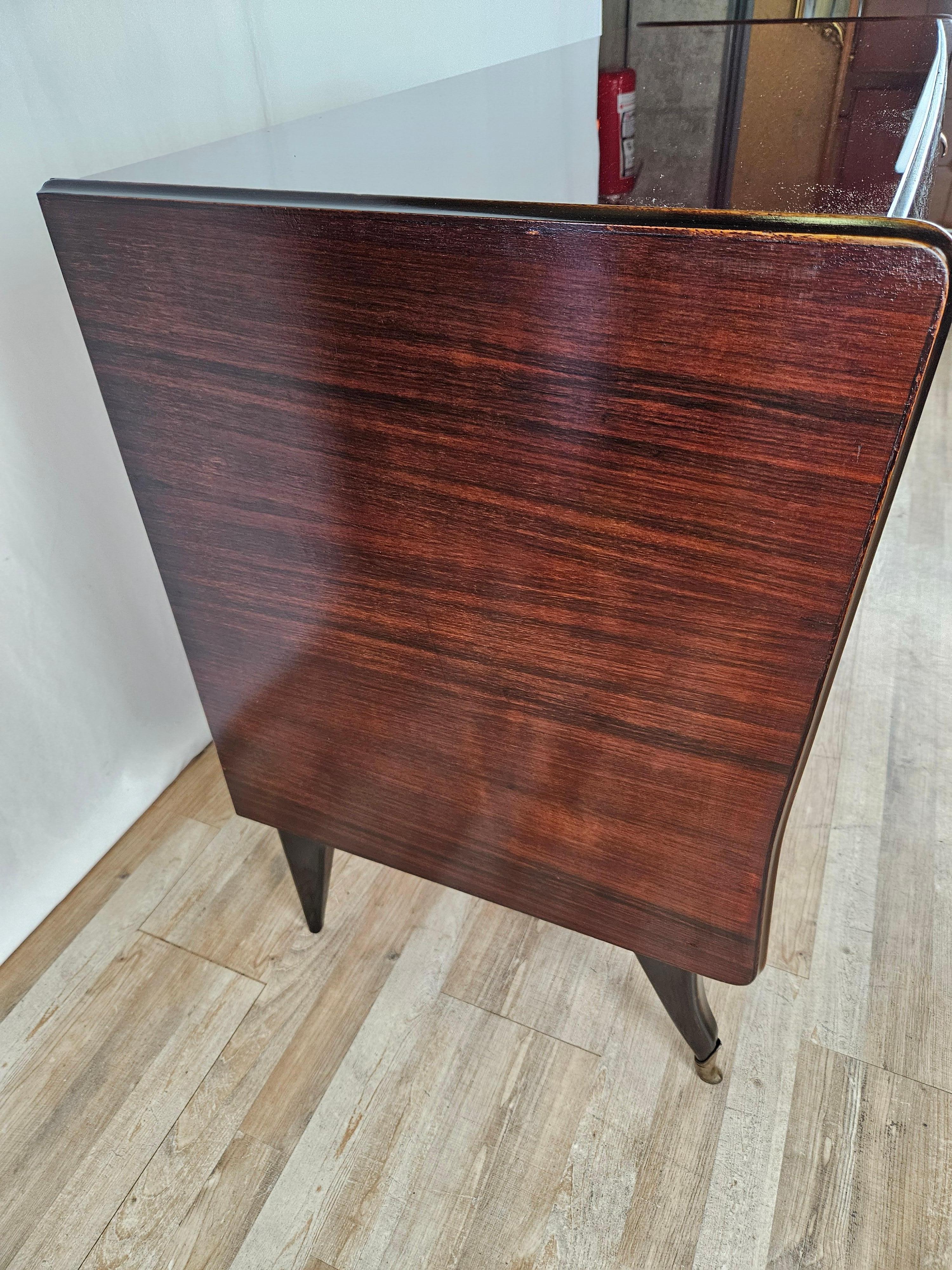 Refined 1950s Art Deco chest of drawers or sideboard upholstered in mahogany burl with carved profiles and rose brass bow handles.

The burgundy glass top is vintage original, note the soft and elegant line that makes the furniture piece a modern