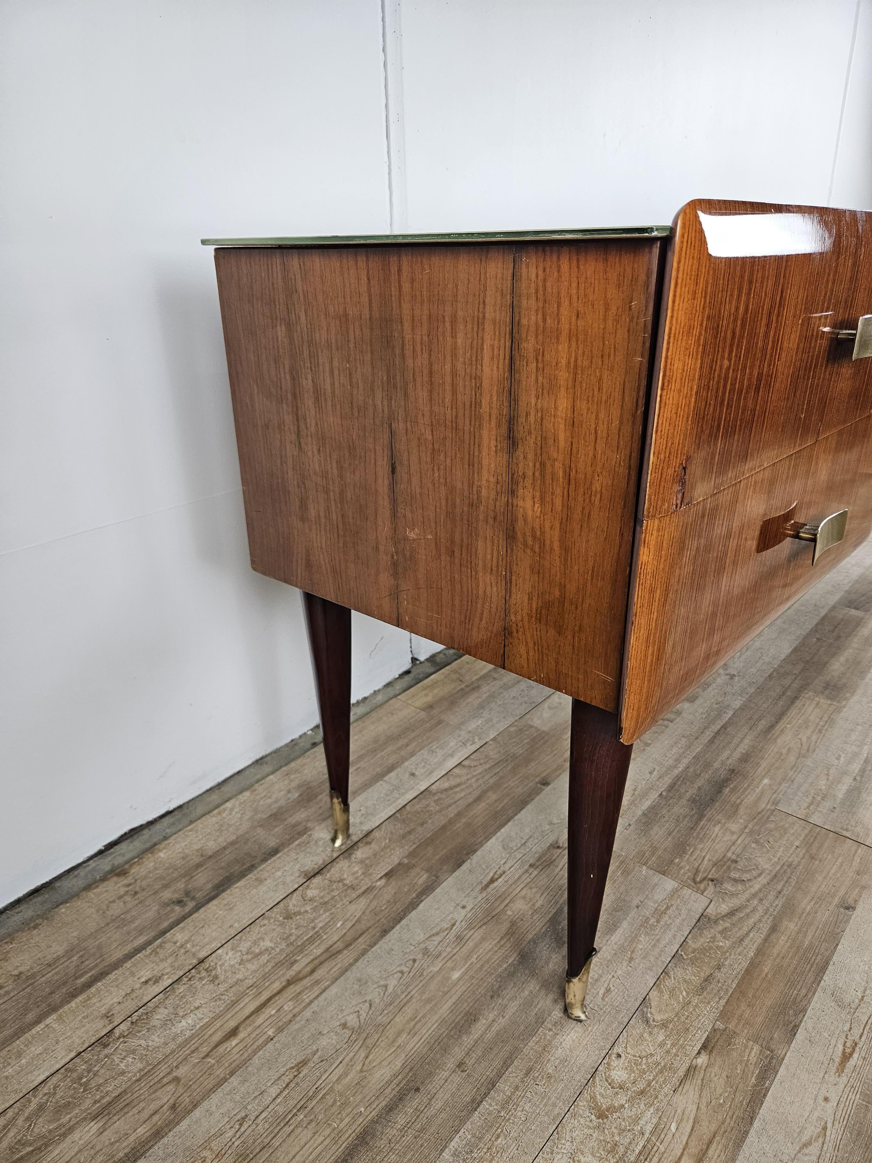 Credenza rivestita in radica di mogano con gambe alte e puntalini finali in ottone, arricchita da un particolare piano in vetro e da un set di maniglie in ottone originali dell'epoca.

Cassettiera lineare, dal design moderno e dalle linee compatte