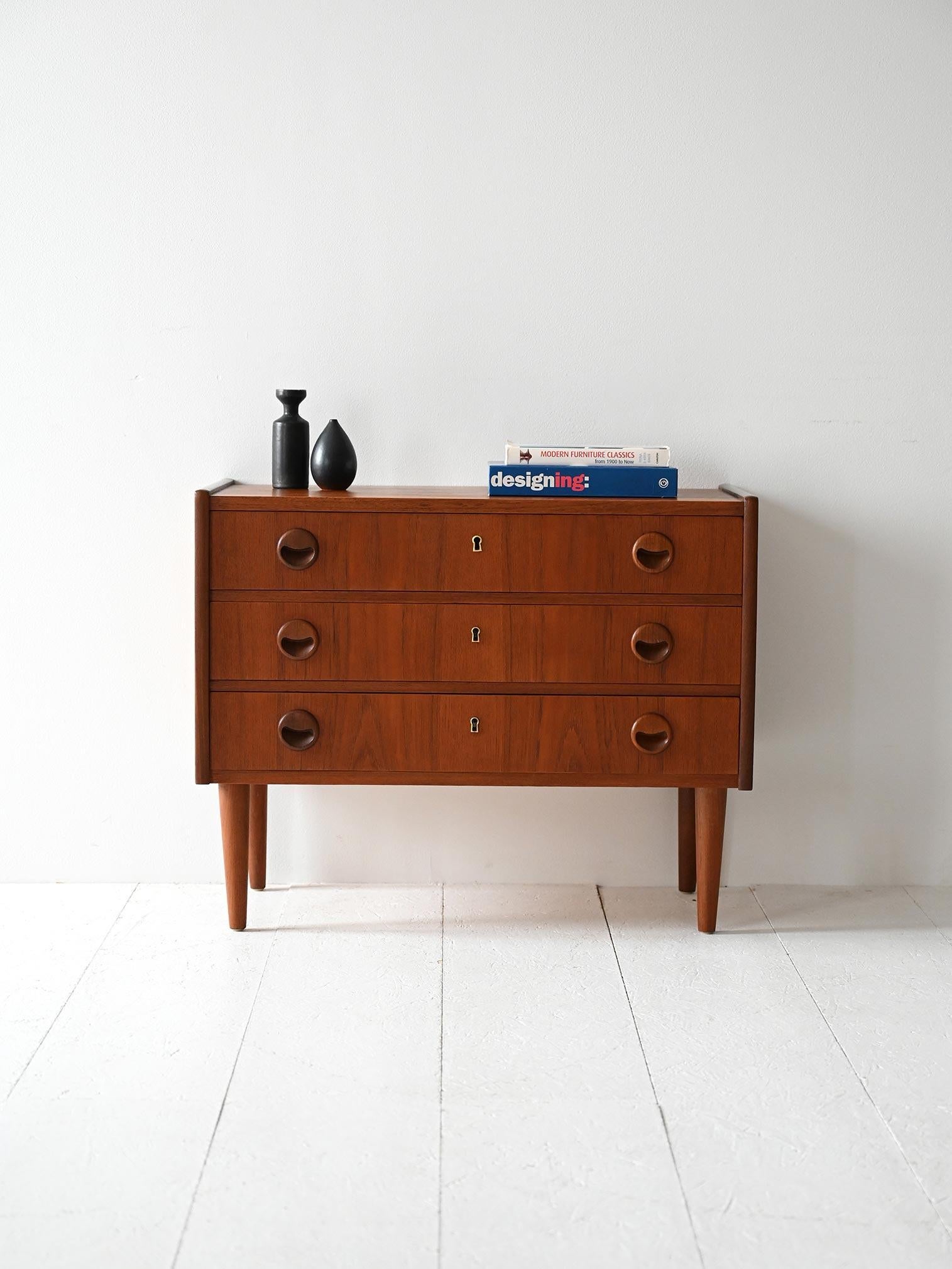 Cassettiera in teak con tre cassetti e maniglie intagliate scultoree, finitura calda e gambe affusolate.

Linee pulite e dettagli scolpiti per una cassettiera scandinava in teak risalente agli anni ’50/’60. I tre cassetti sono dotati di maniglie